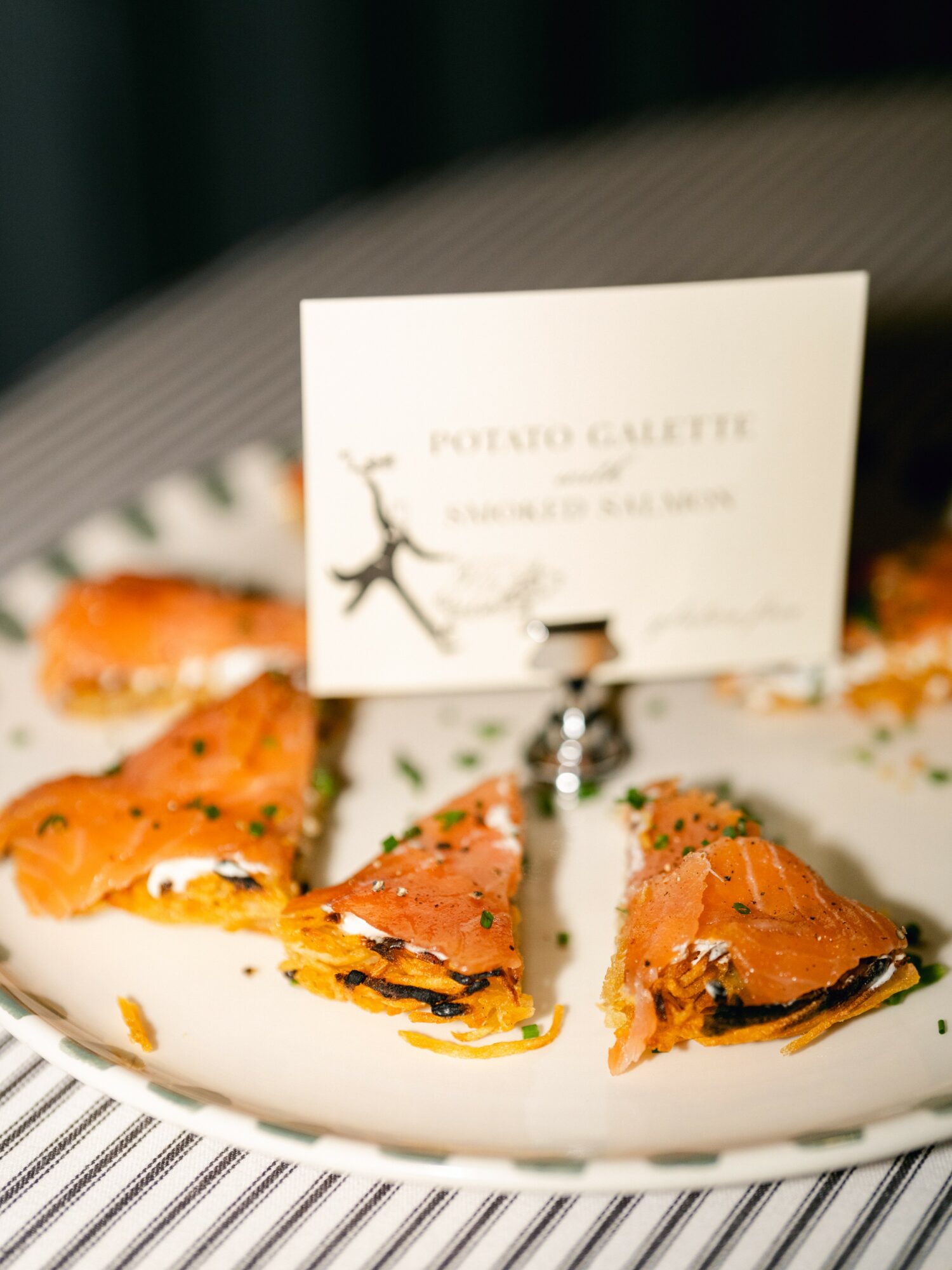 Sliced salmon on a white plate with a business card in the background, on a striped tablecloth.