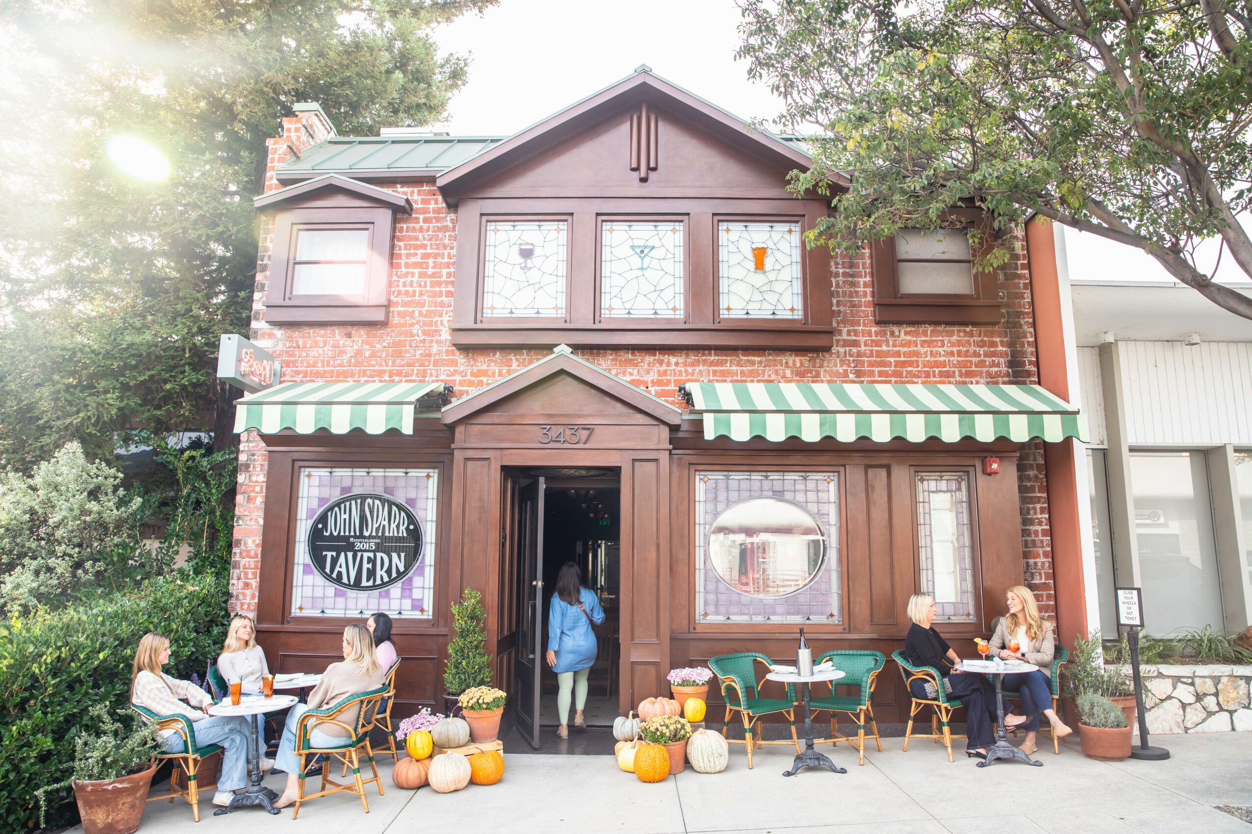 Brick building with striped awnings, outdoor seating, pumpkins, and trees, with people sitting and walking outside.
