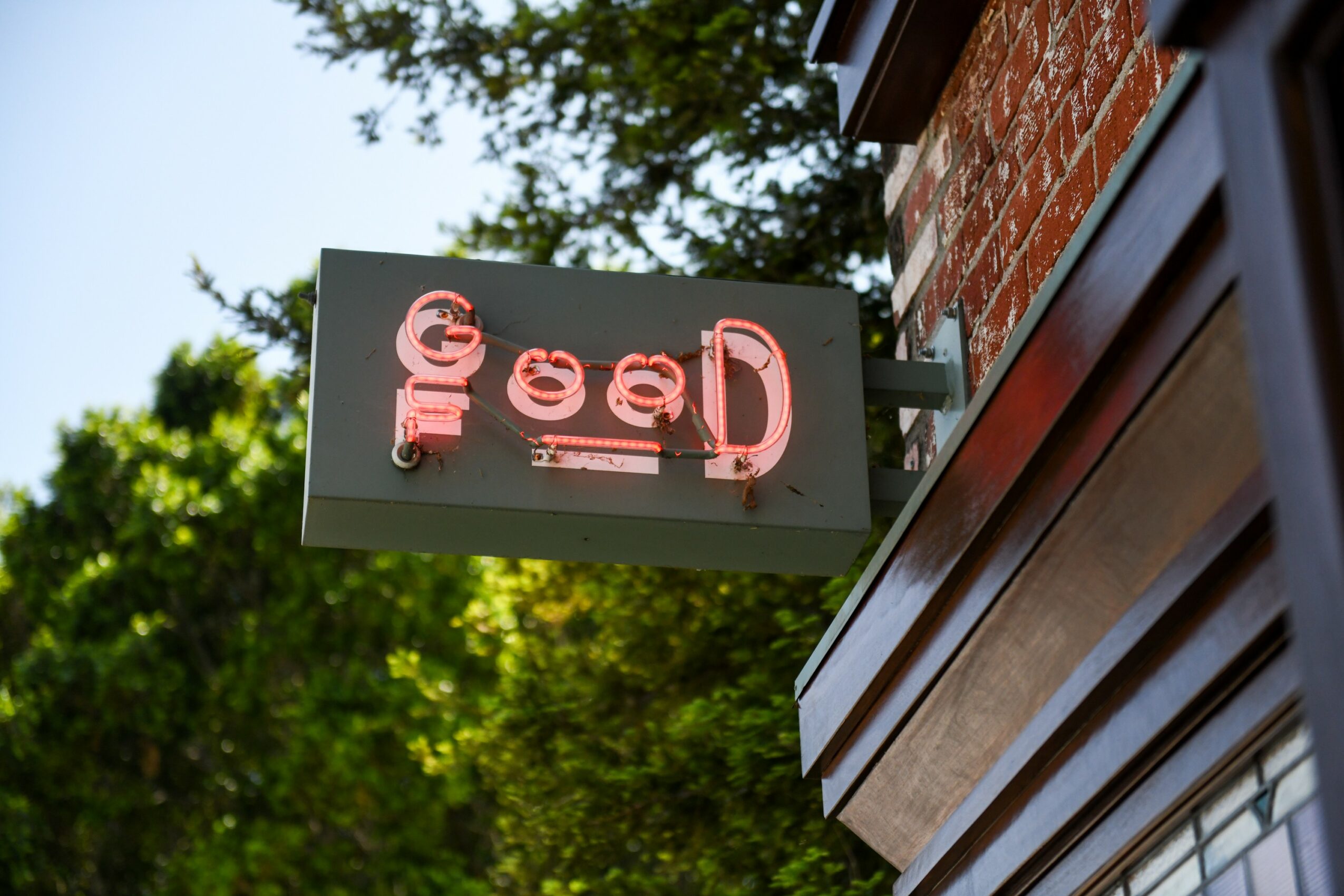 Neon sign with partially visible red and white text, mounted on a brick wall outside a building.