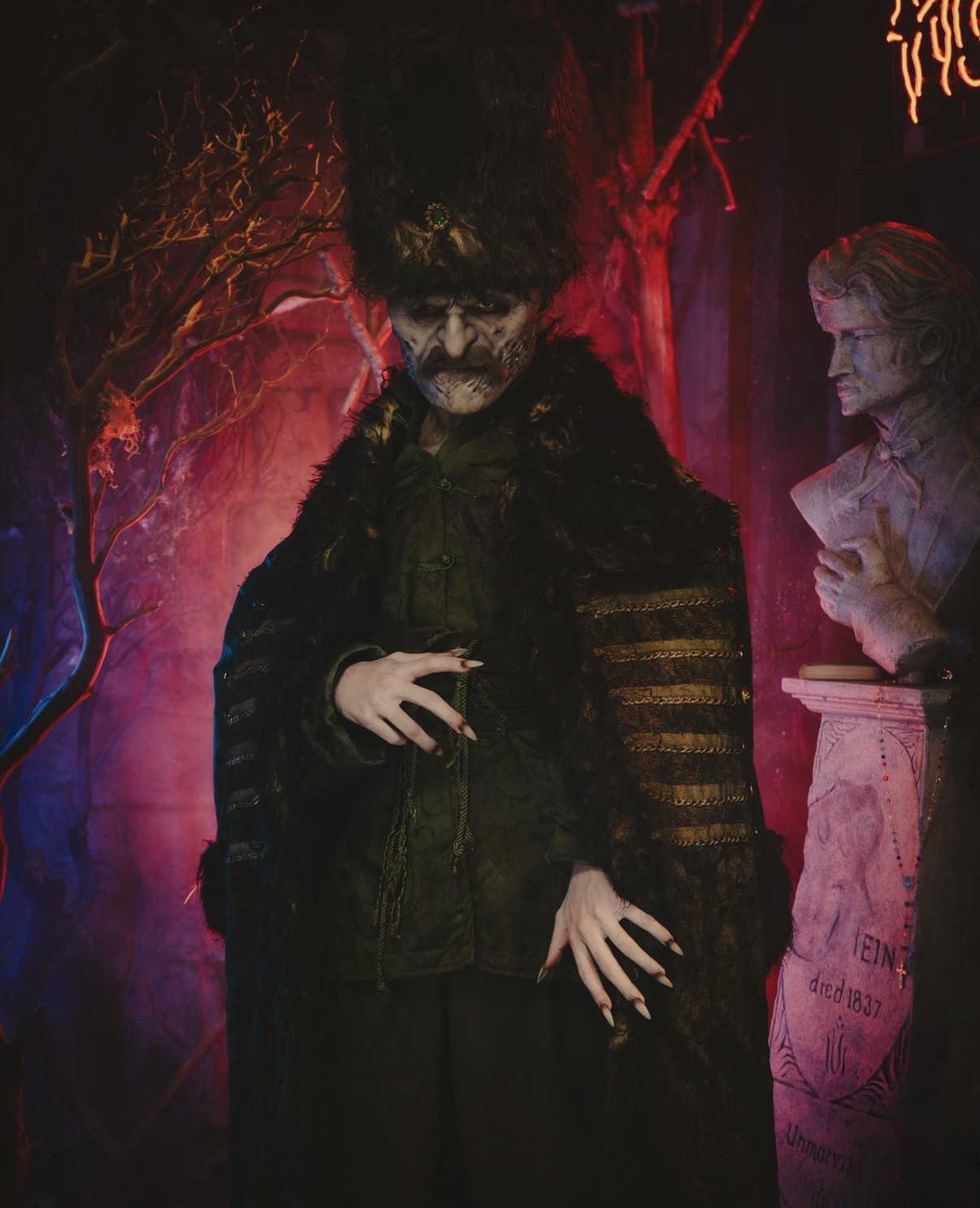Person with dark hair and mustache wearing dark clothing, standing in front of a red and purple background.