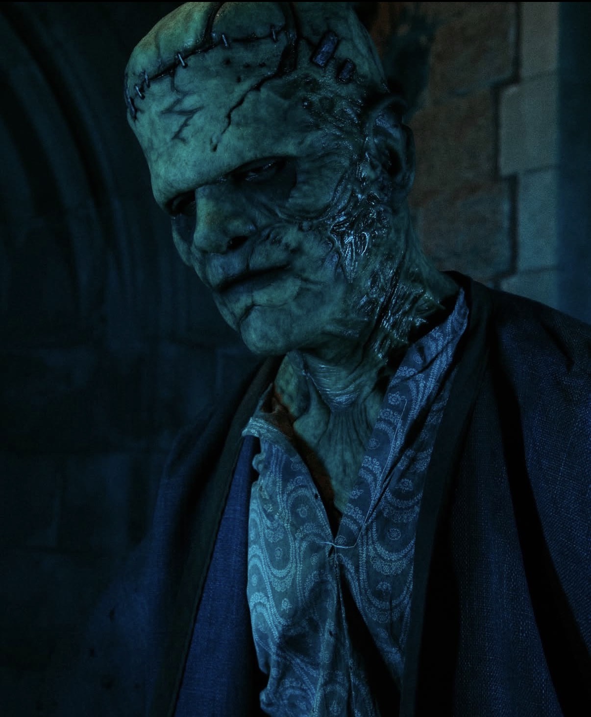 Close-up of a creature with textured, cracked skin and a stern expression, wearing a patterned shirt and dark jacket.