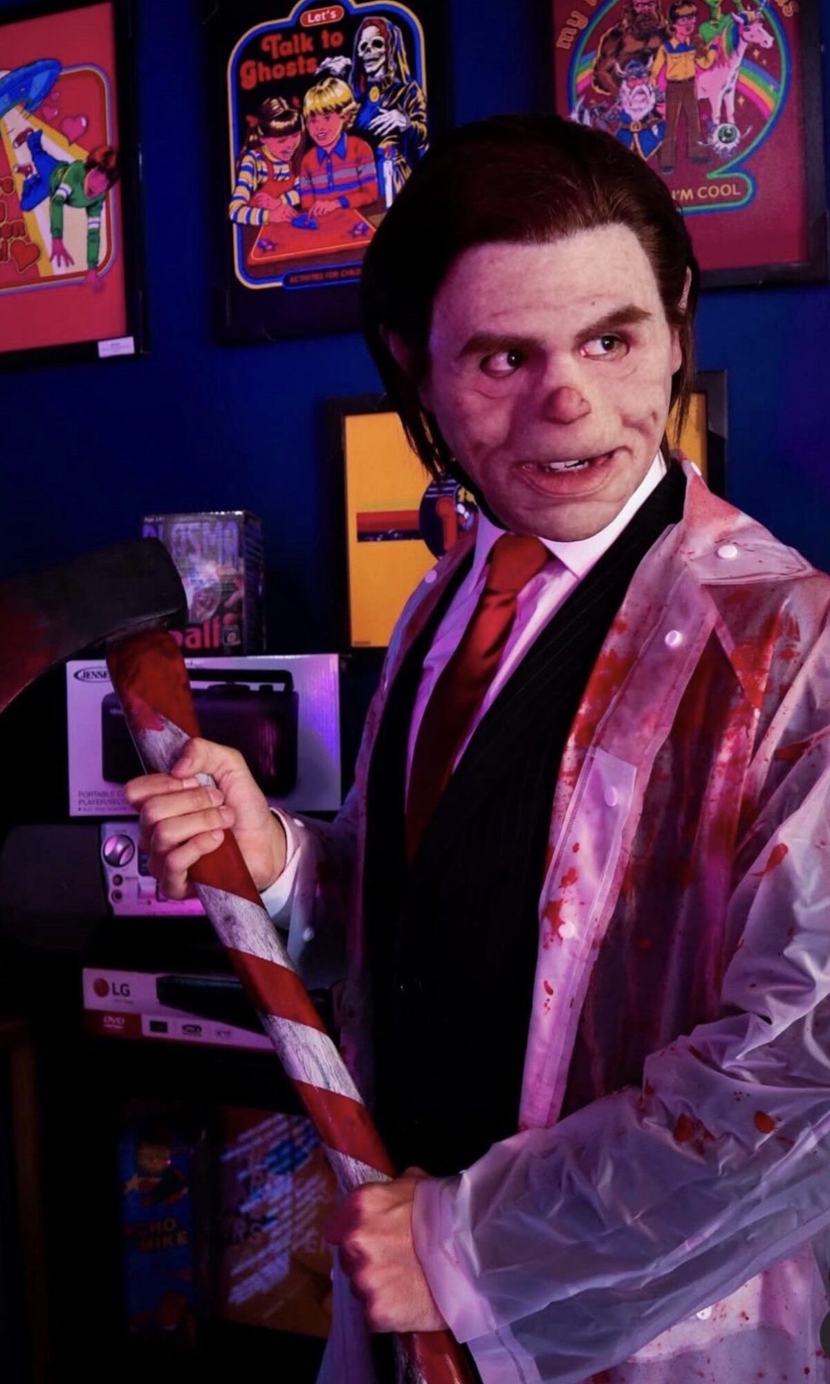 Person dressed as a character with makeup, holding a candy cane, standing in front of colorful posters.