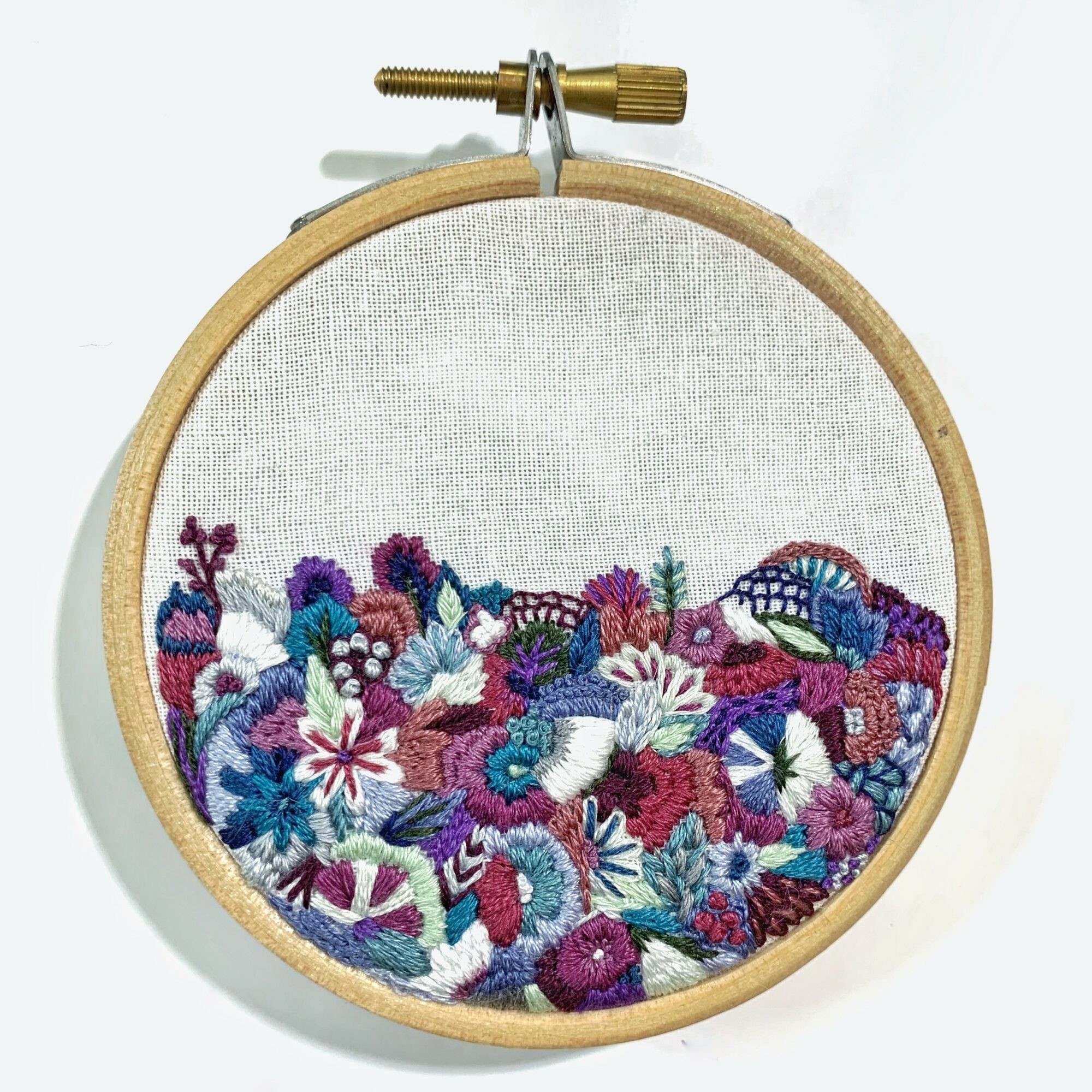 Embroidery hoop with colorful floral design on white fabric, featuring various flowers in purple, pink, blue, and white.