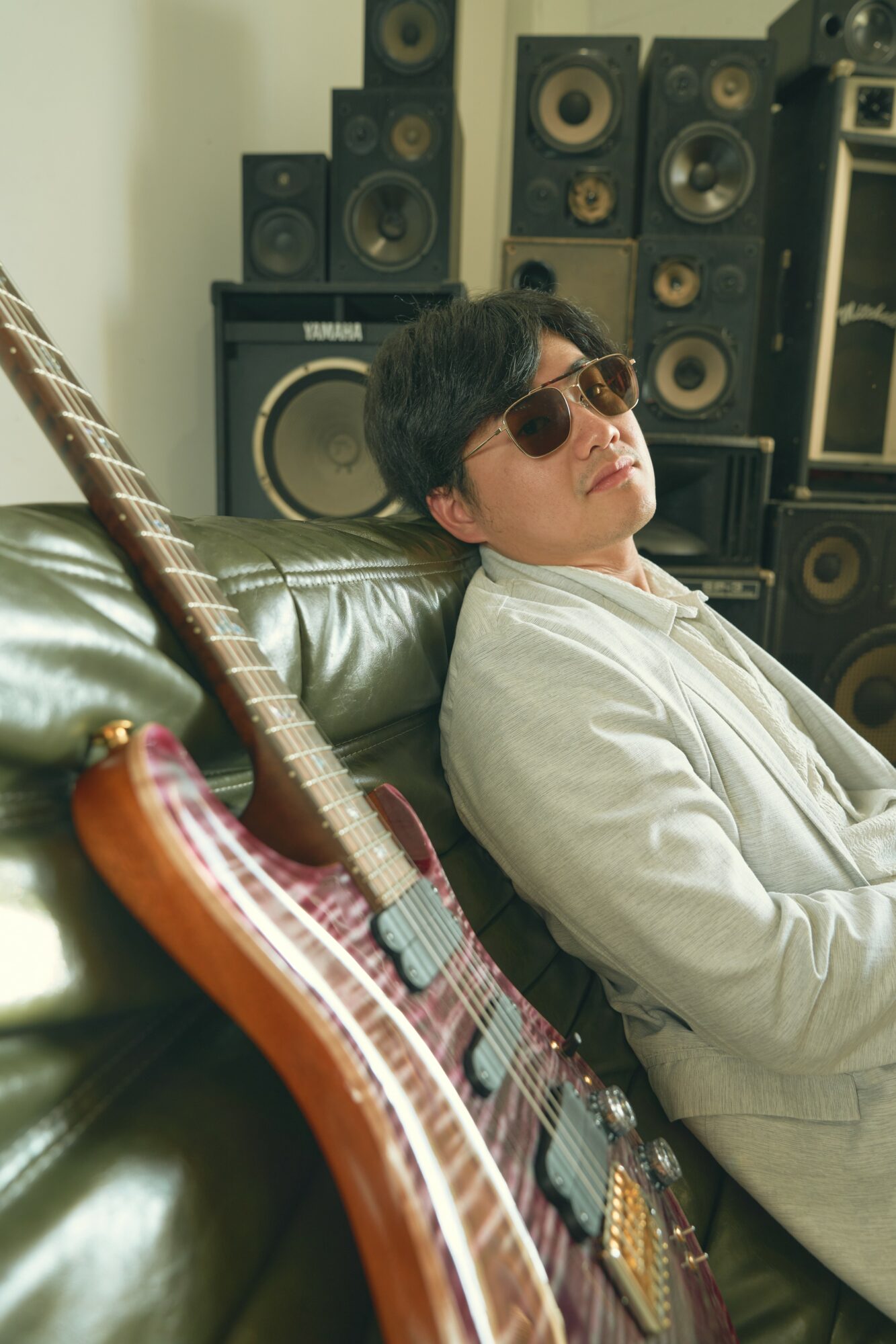 Person with sunglasses leaning back on a green leather sofa, surrounded by large speakers and audio equipment.