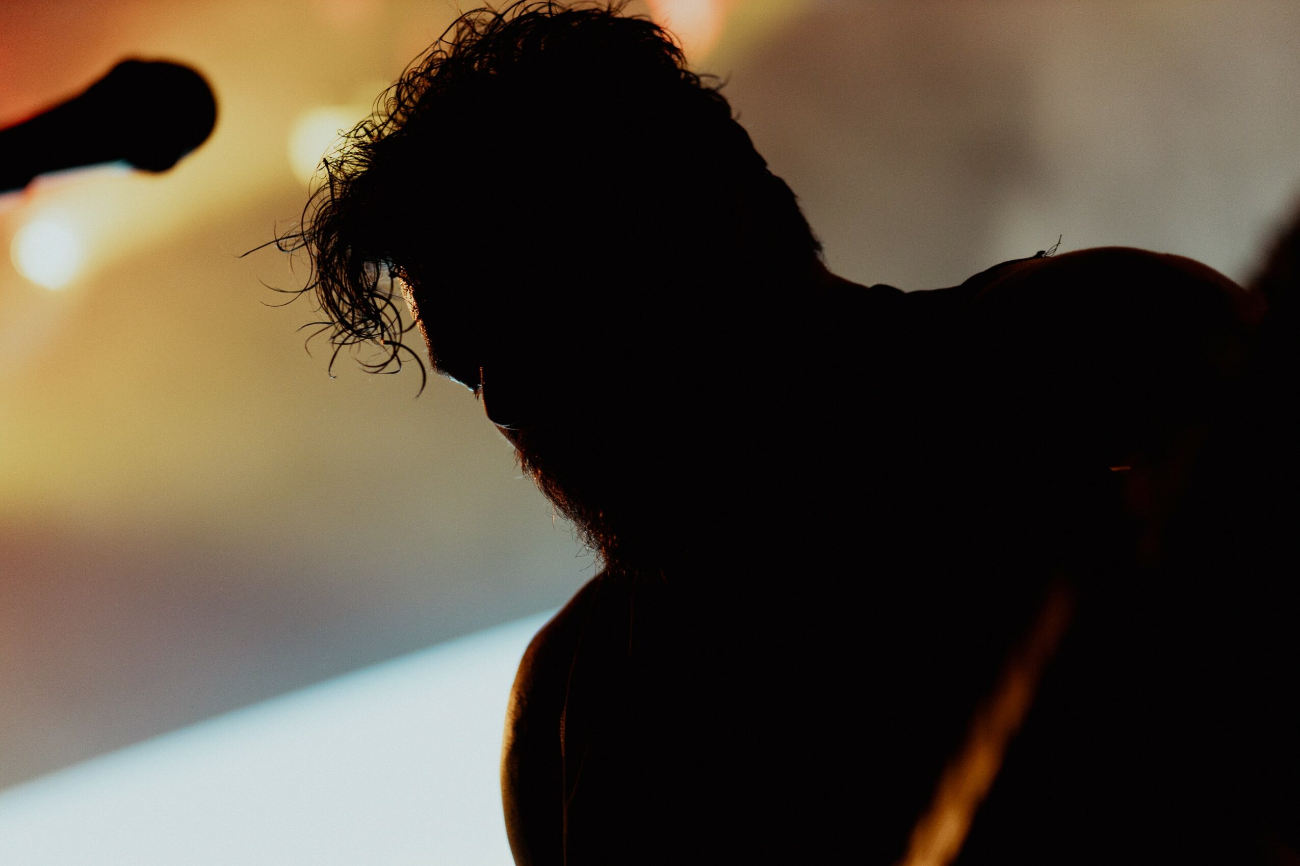 Silhouette of a person with curly hair against a blurred background with warm lighting.