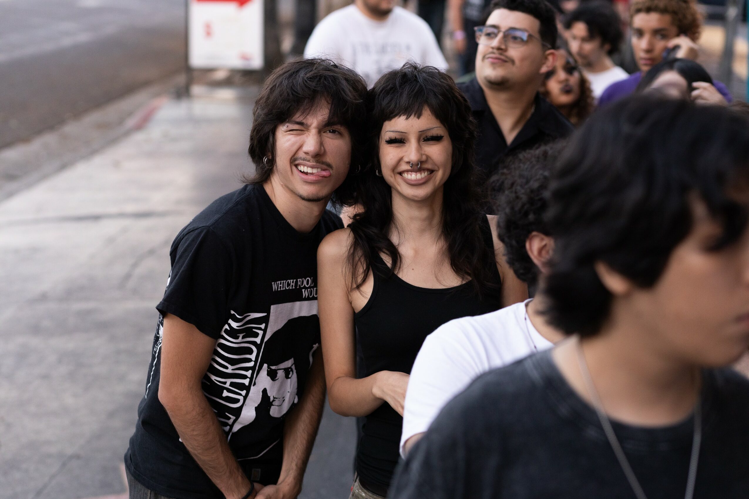 Group of people standing outdoors, smiling, with two people in the foreground smiling at the camera.
