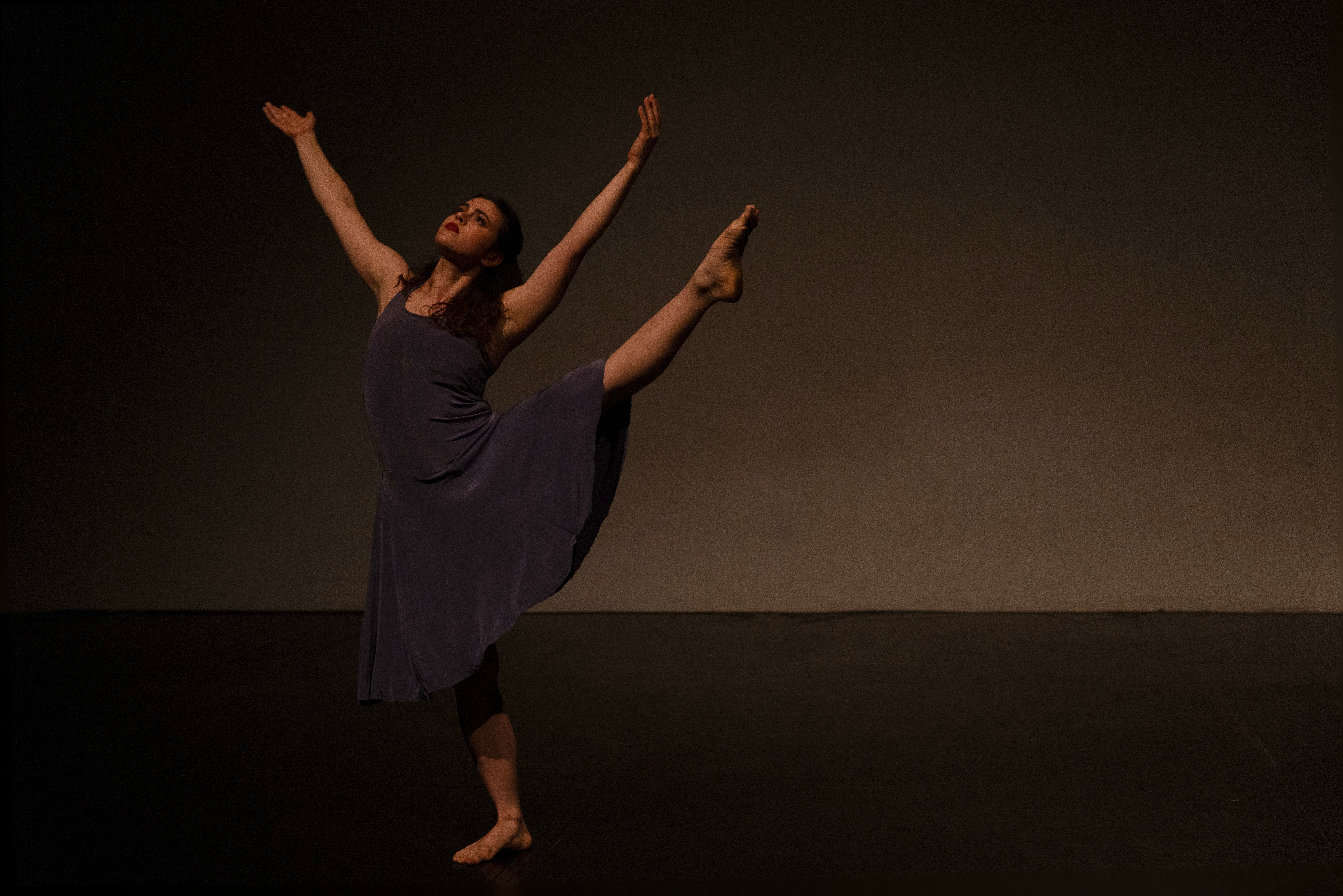 Ballet dancer performing a high leg extension on stage with arms raised.