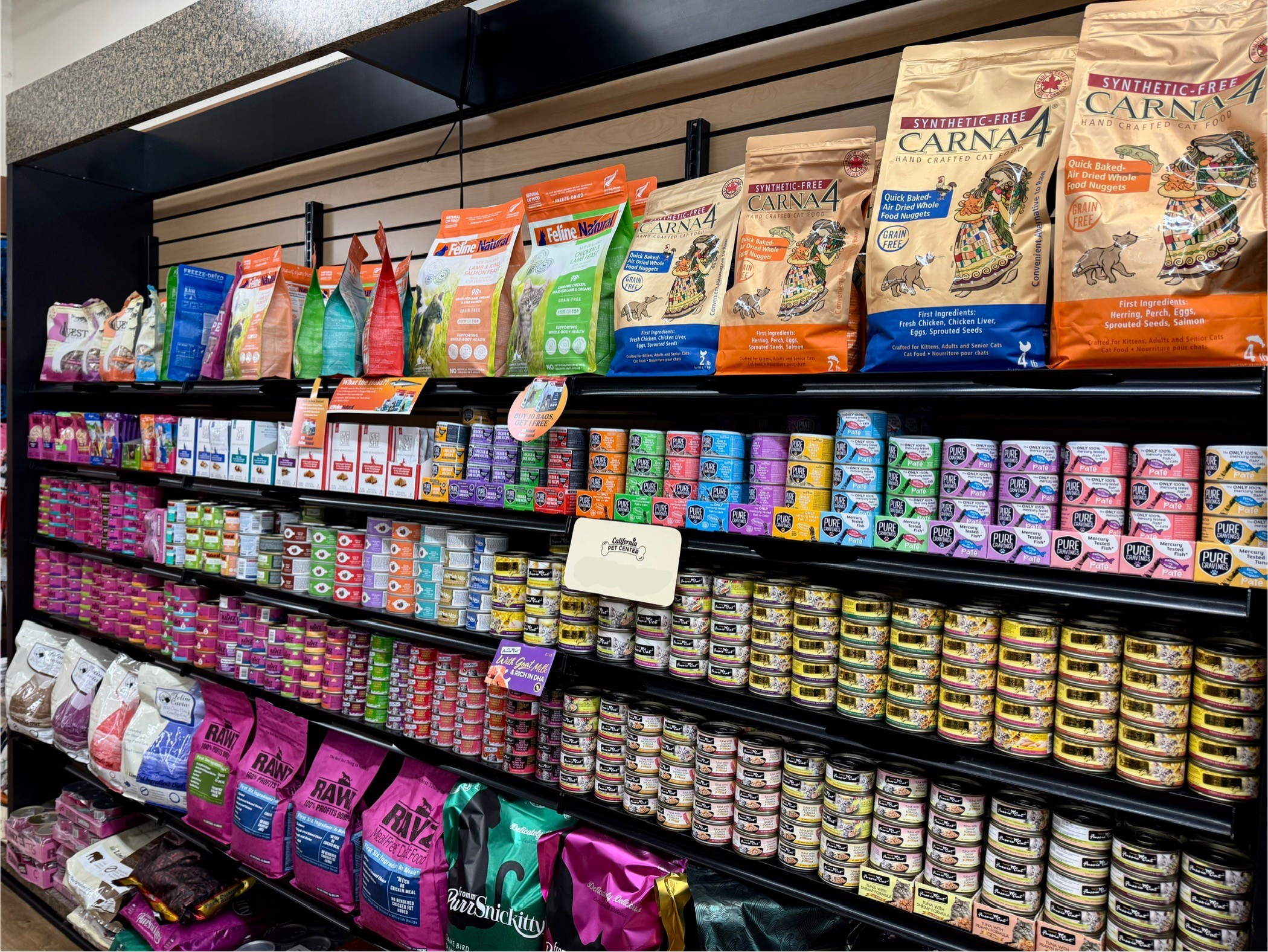 Shelves stocked with pet food bags and cans, organized by brand and type, in a store aisle.