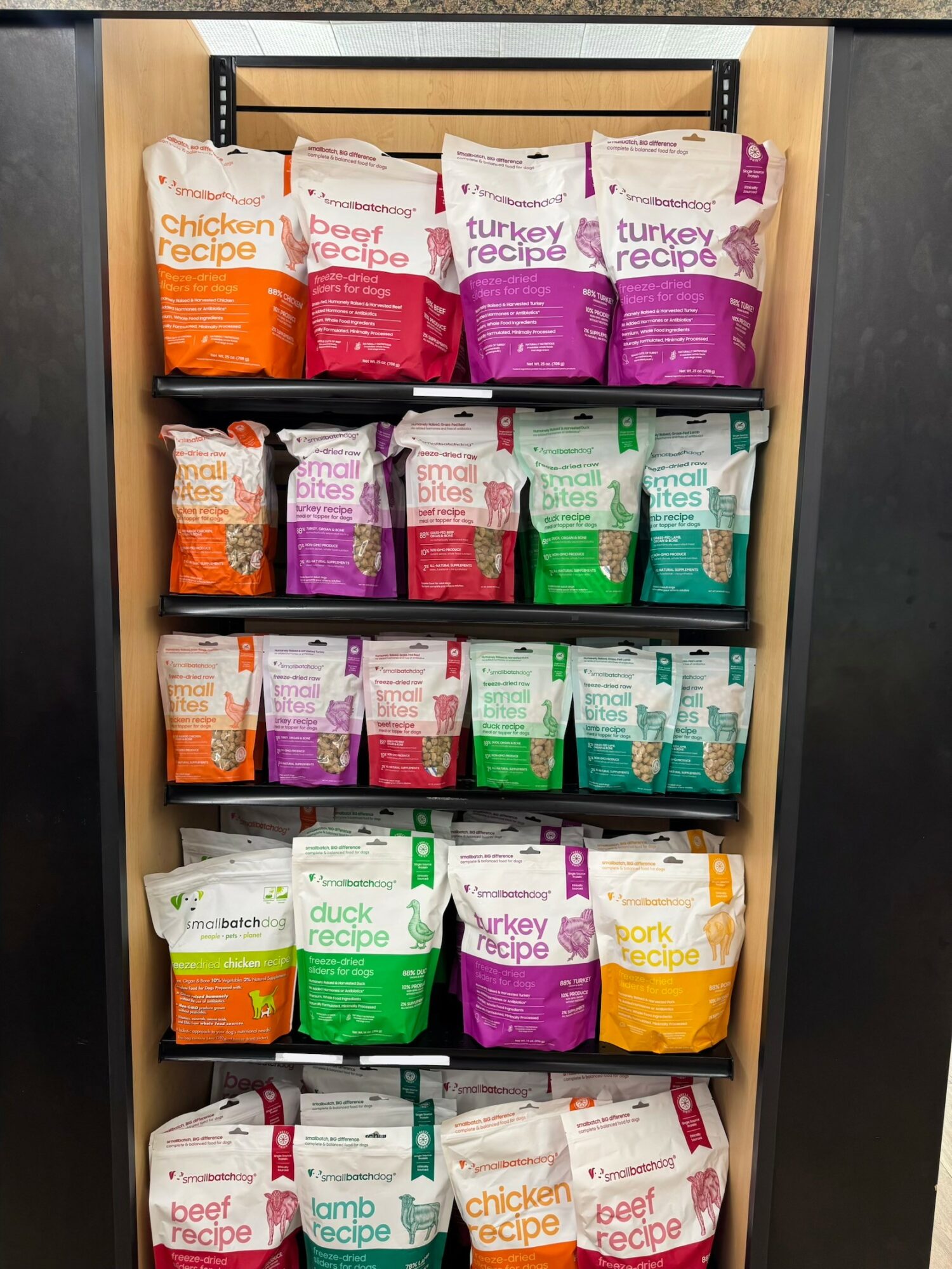 Shelves with bags of pet food in various colors and labels, organized in rows inside a wooden cabinet.