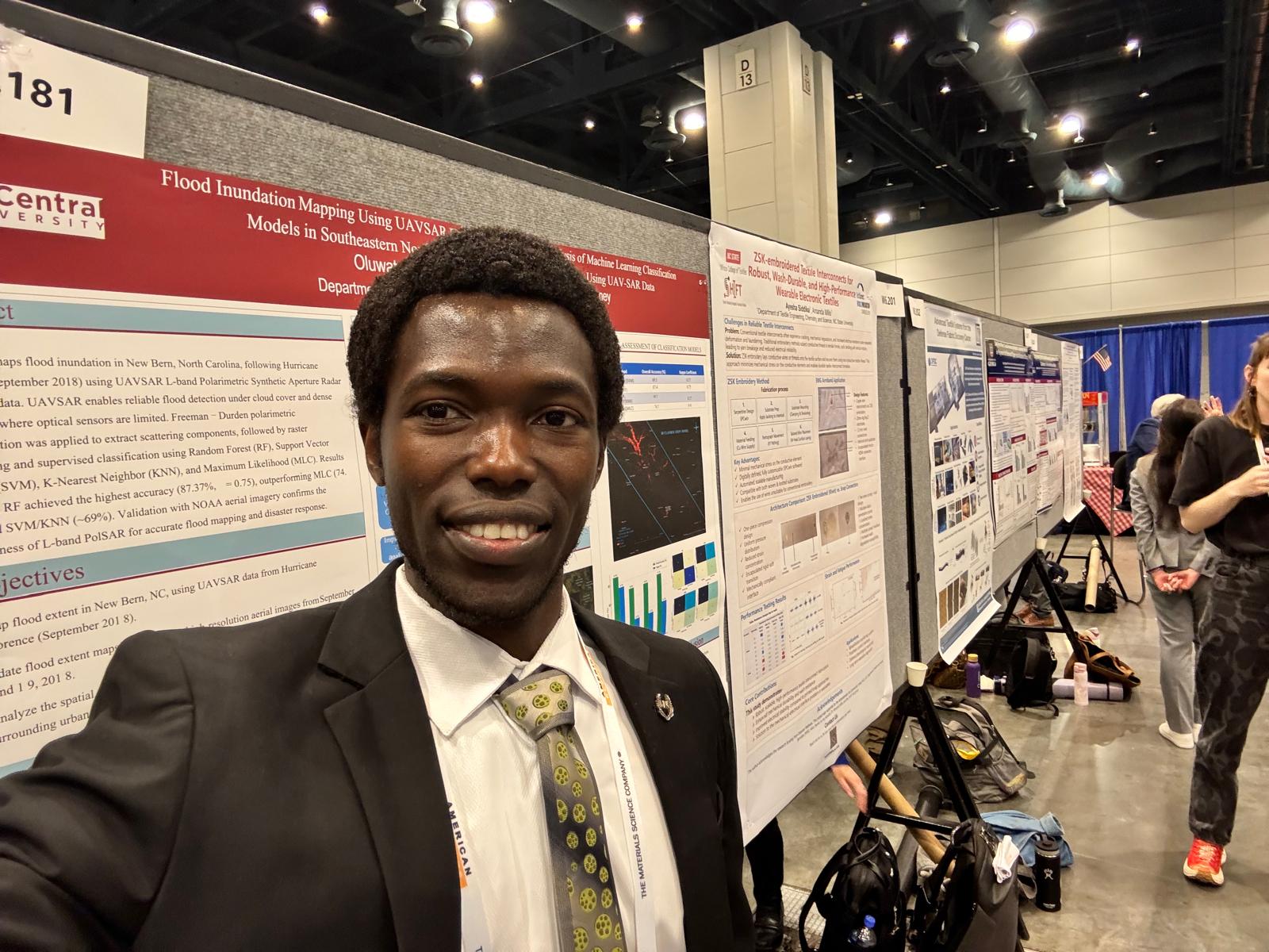 Man in suit taking a selfie at a conference with research posters in the background.