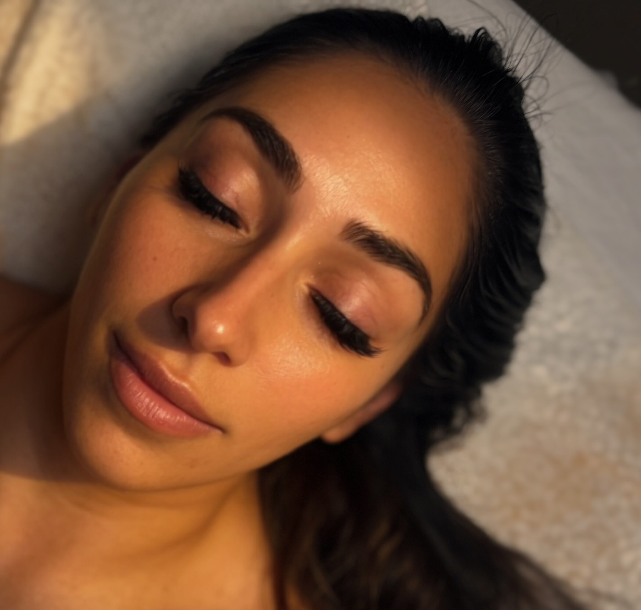 Close-up of a woman with closed eyes, makeup, and dark hair lying down.