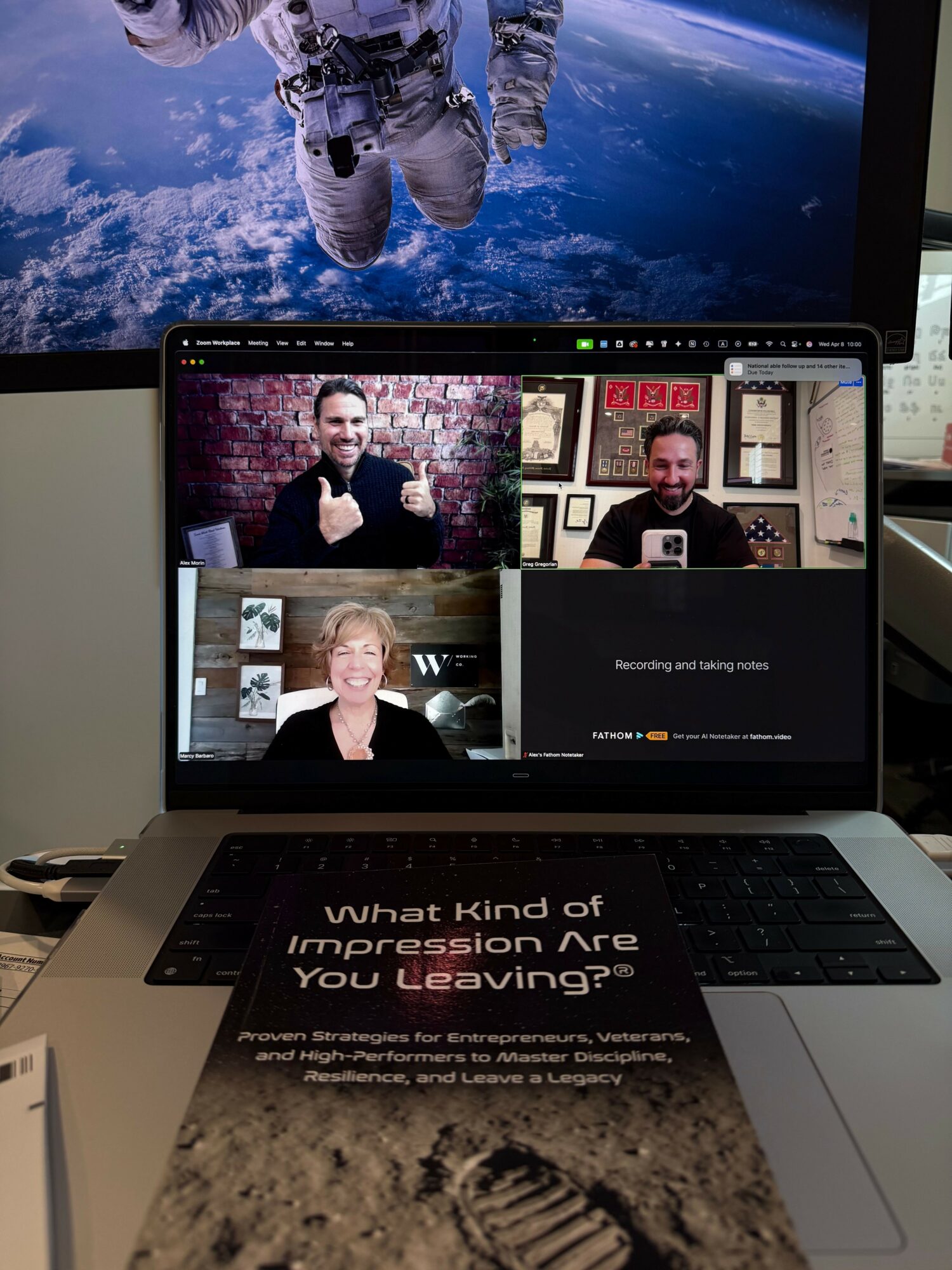 Laptop screen shows four people in a video call, with a space-themed background behind the astronaut image. Text on laptop reads about leaving a legacy.