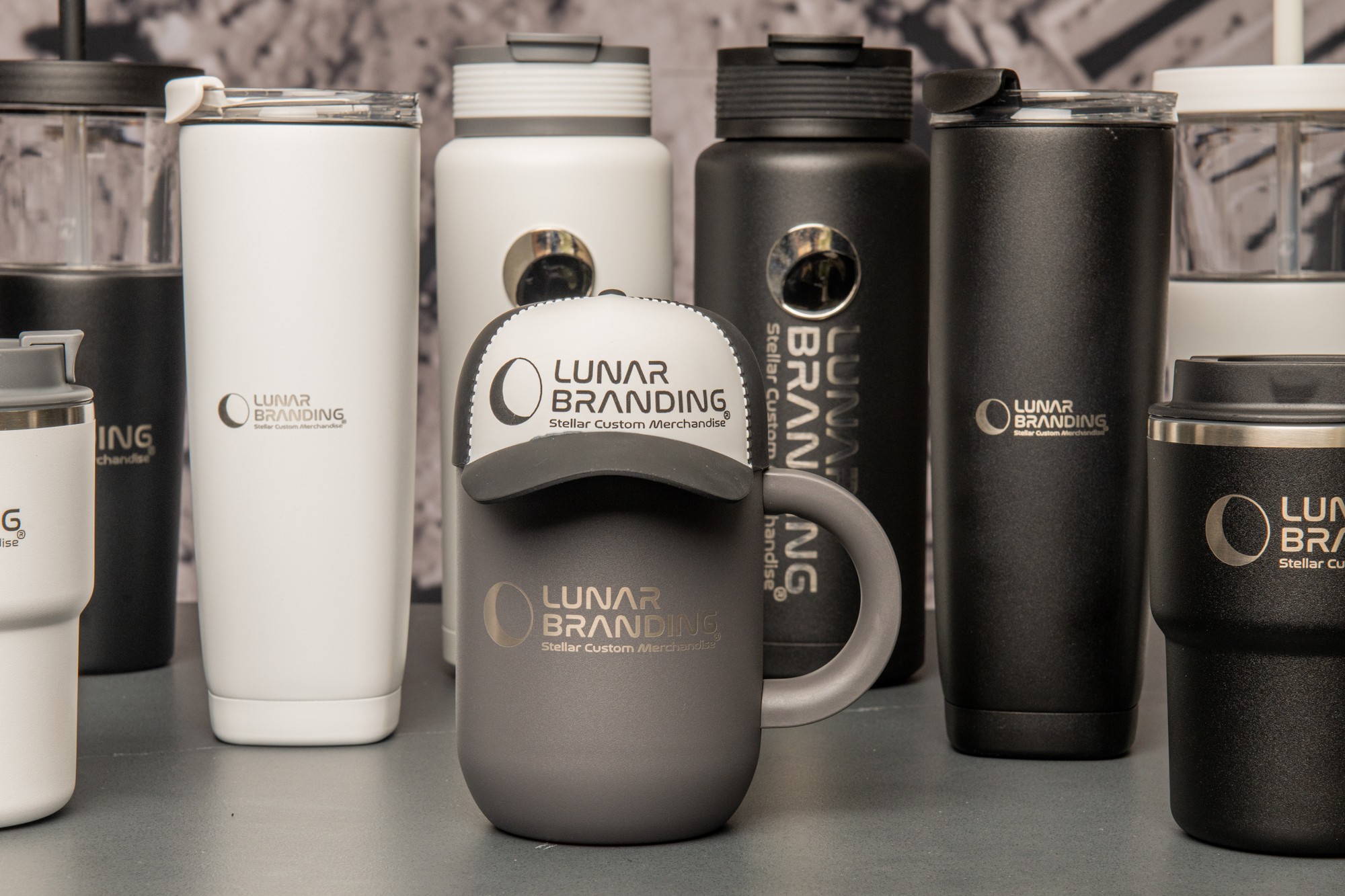 Collection of black and white travel mugs and a cap with lunar branding on a table.