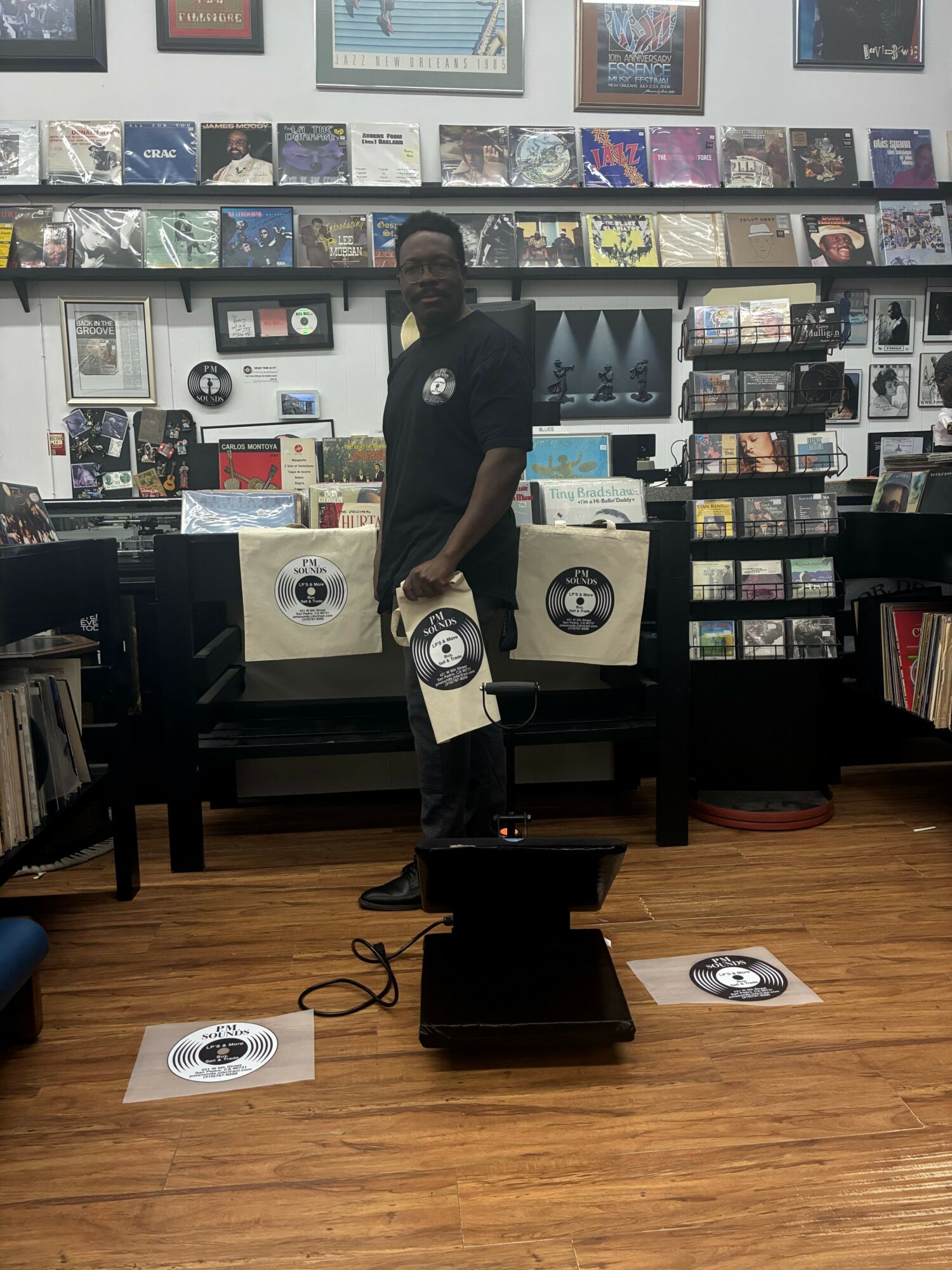 Person standing in record store, surrounded by vinyl records and shelves, holding a vinyl record, with a display of records behind.