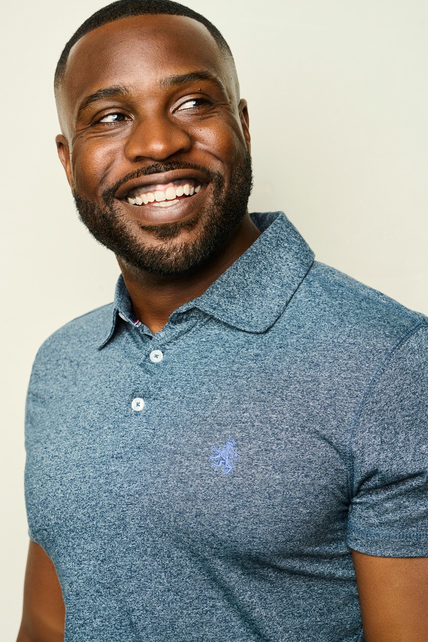 Smiling man with a beard wearing a blue polo shirt, looking to the side.