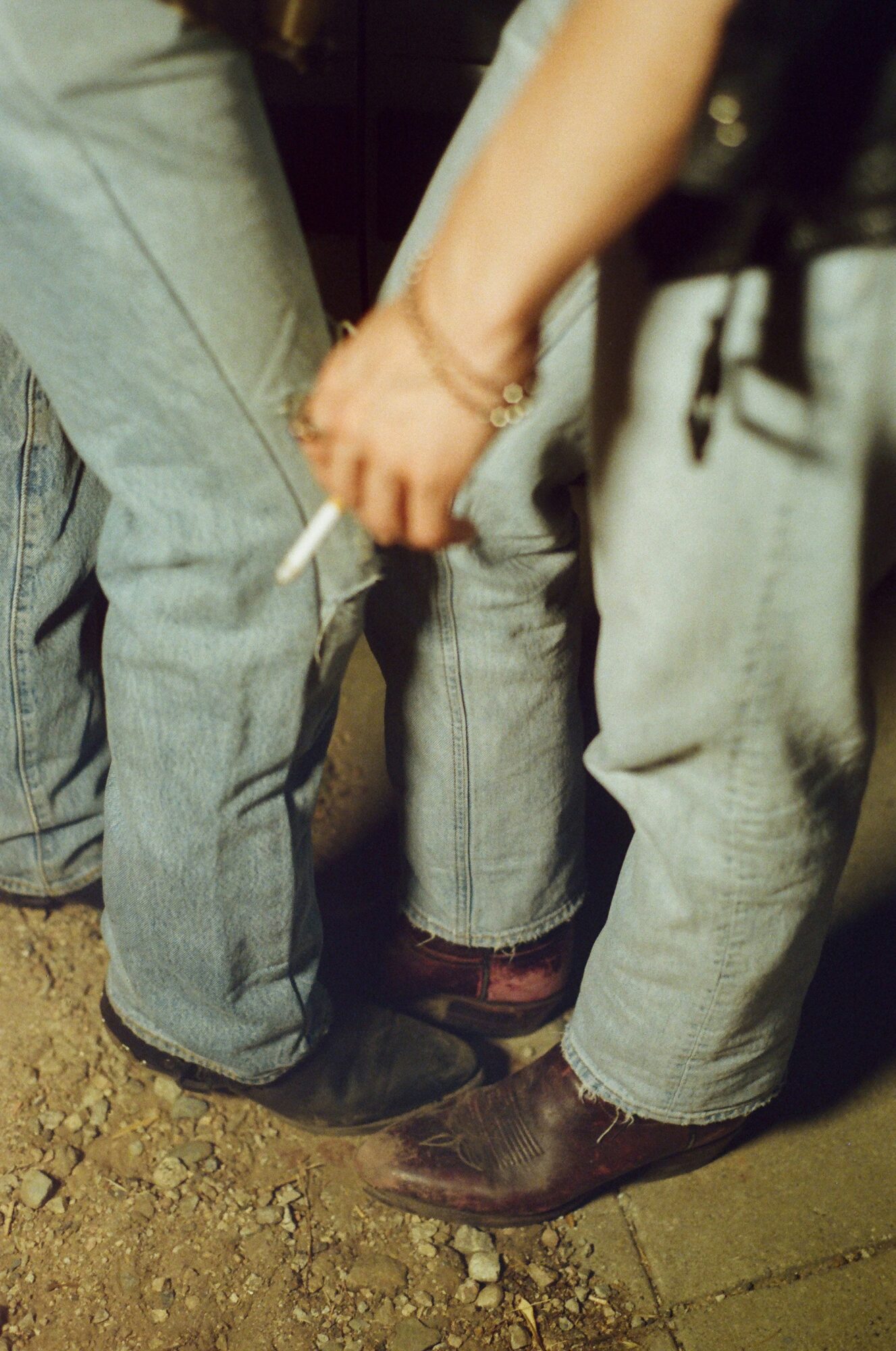 Two people hold hands, standing close on a dirt ground, wearing jeans and boots.