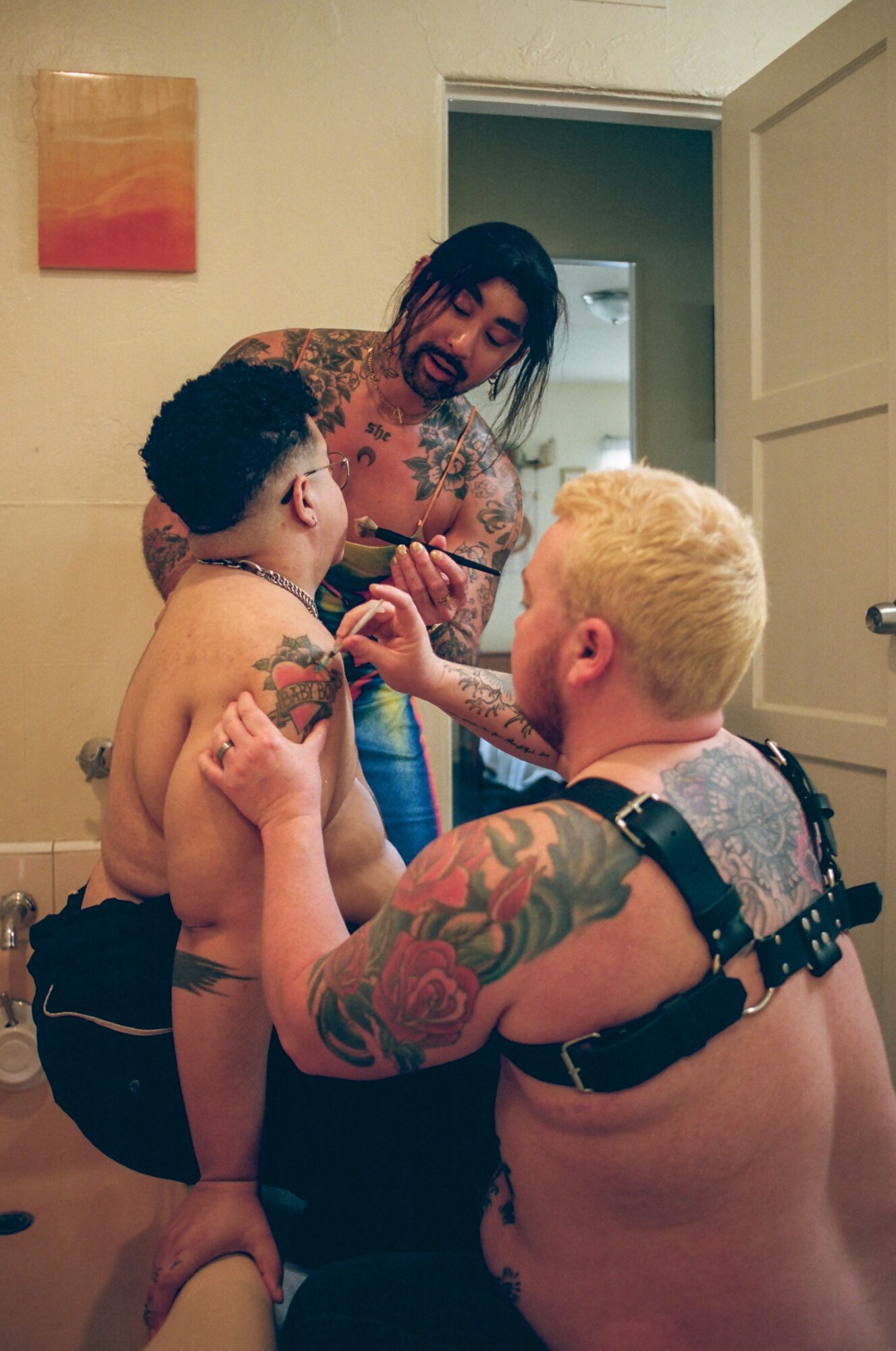 Tattooed woman with dark hair and two shirtless children with tattoos in a room, one child with blonde hair and the other with dark hair.