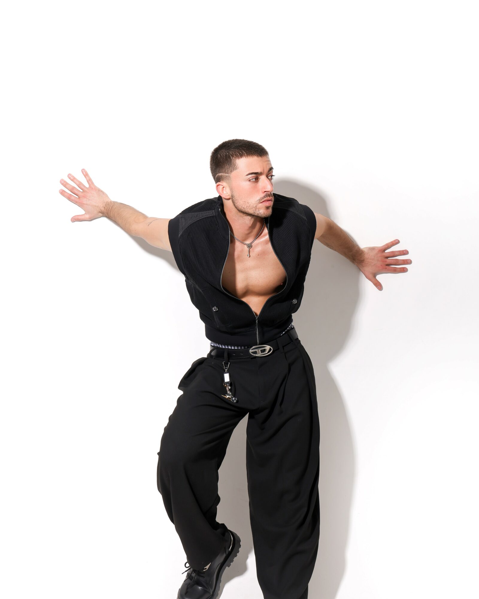 Person in black outfit leaning forward with arms extended sideways against a white background.