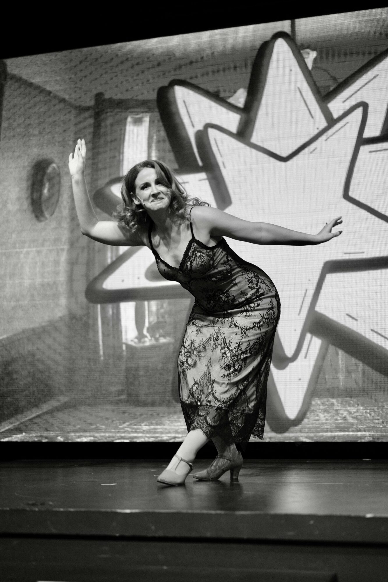 Woman in a lace dress dancing on stage with a star-shaped backdrop behind her.
