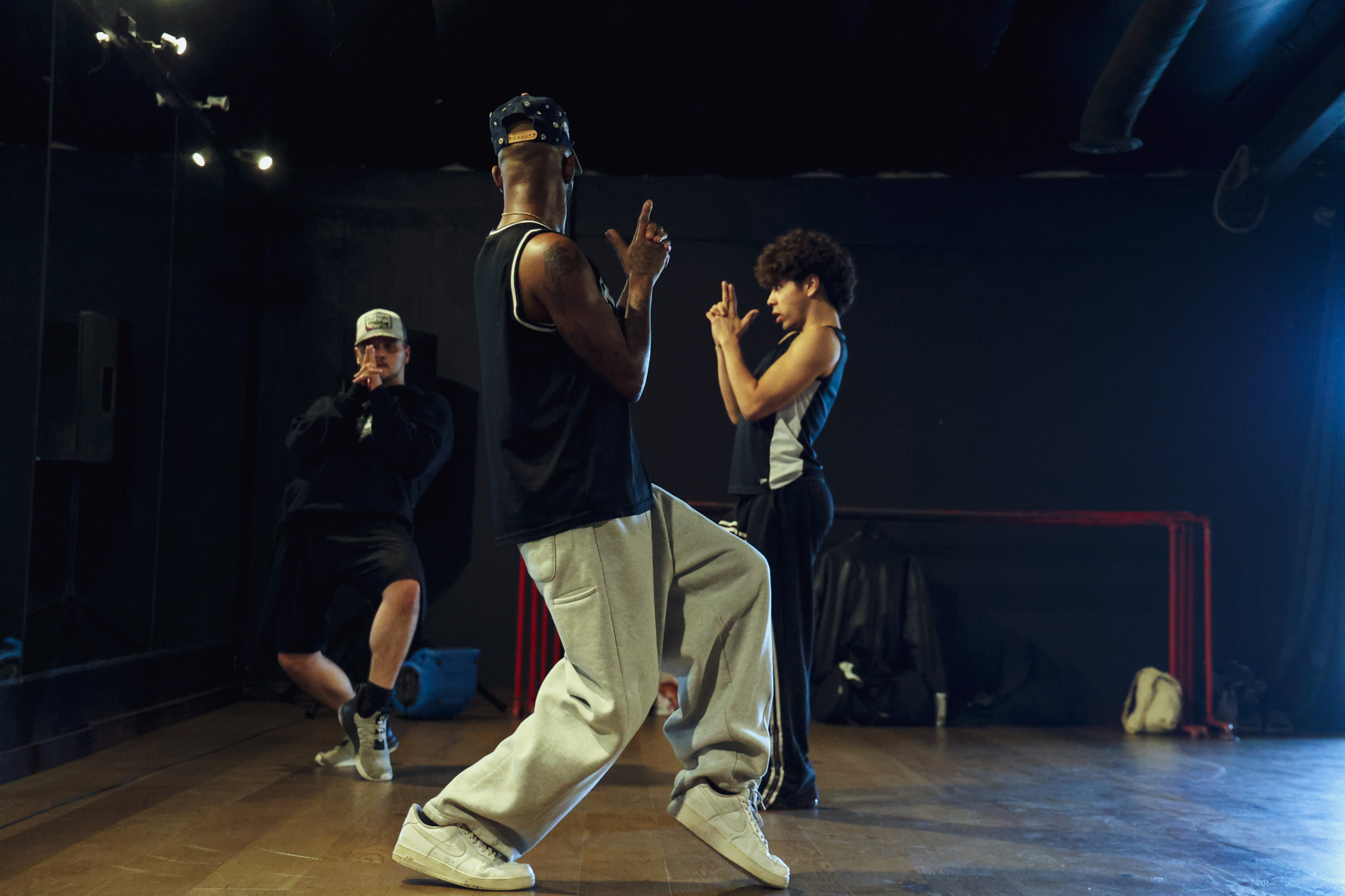 Three people dancing in a dark room with a wooden floor, illuminated by blue and white lights.