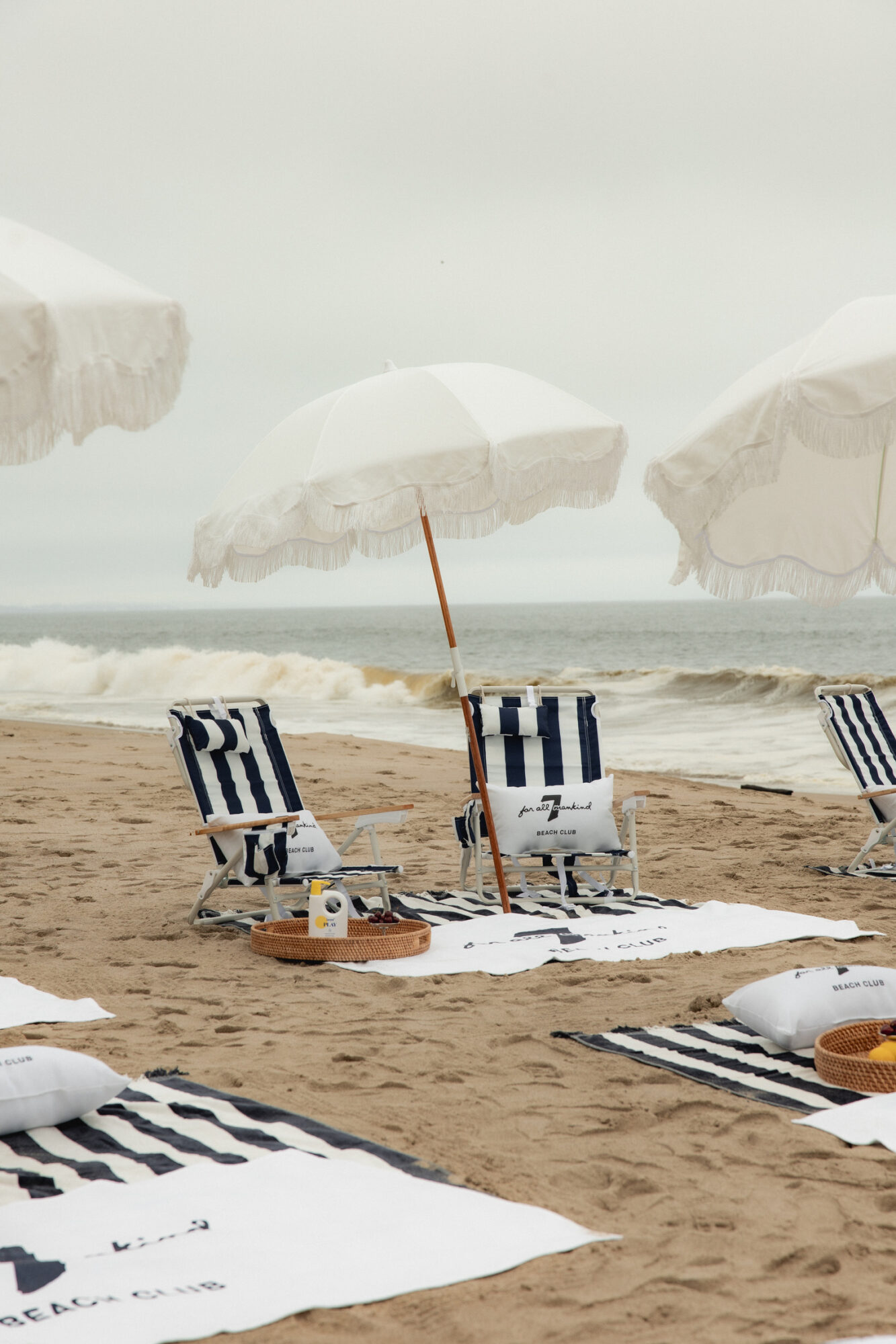 Beach scene with striped chairs, umbrellas, and towels on sand near the ocean, overcast sky, calm waves.