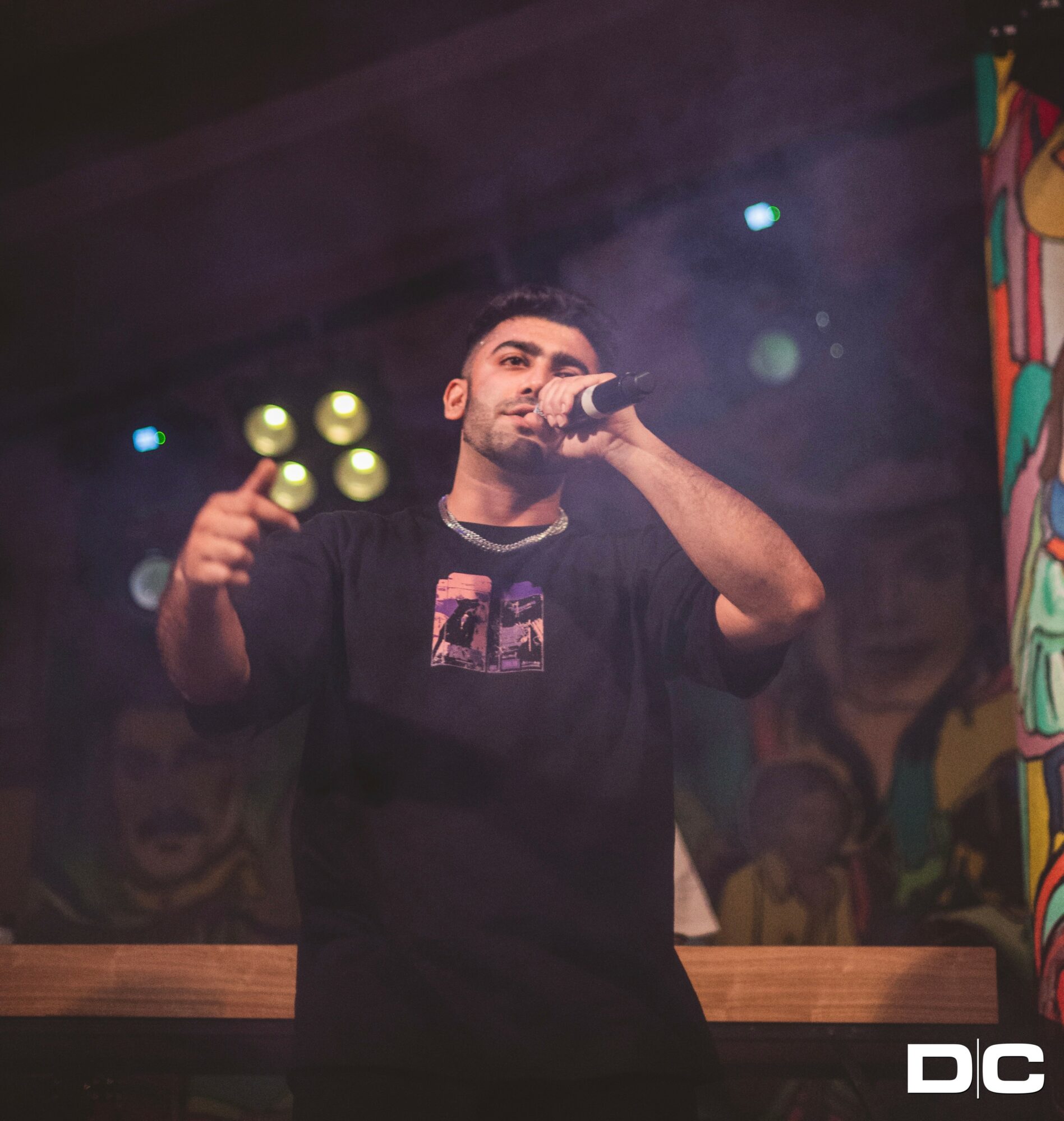 Male performer holding microphone on stage with colorful background and lighting effects.