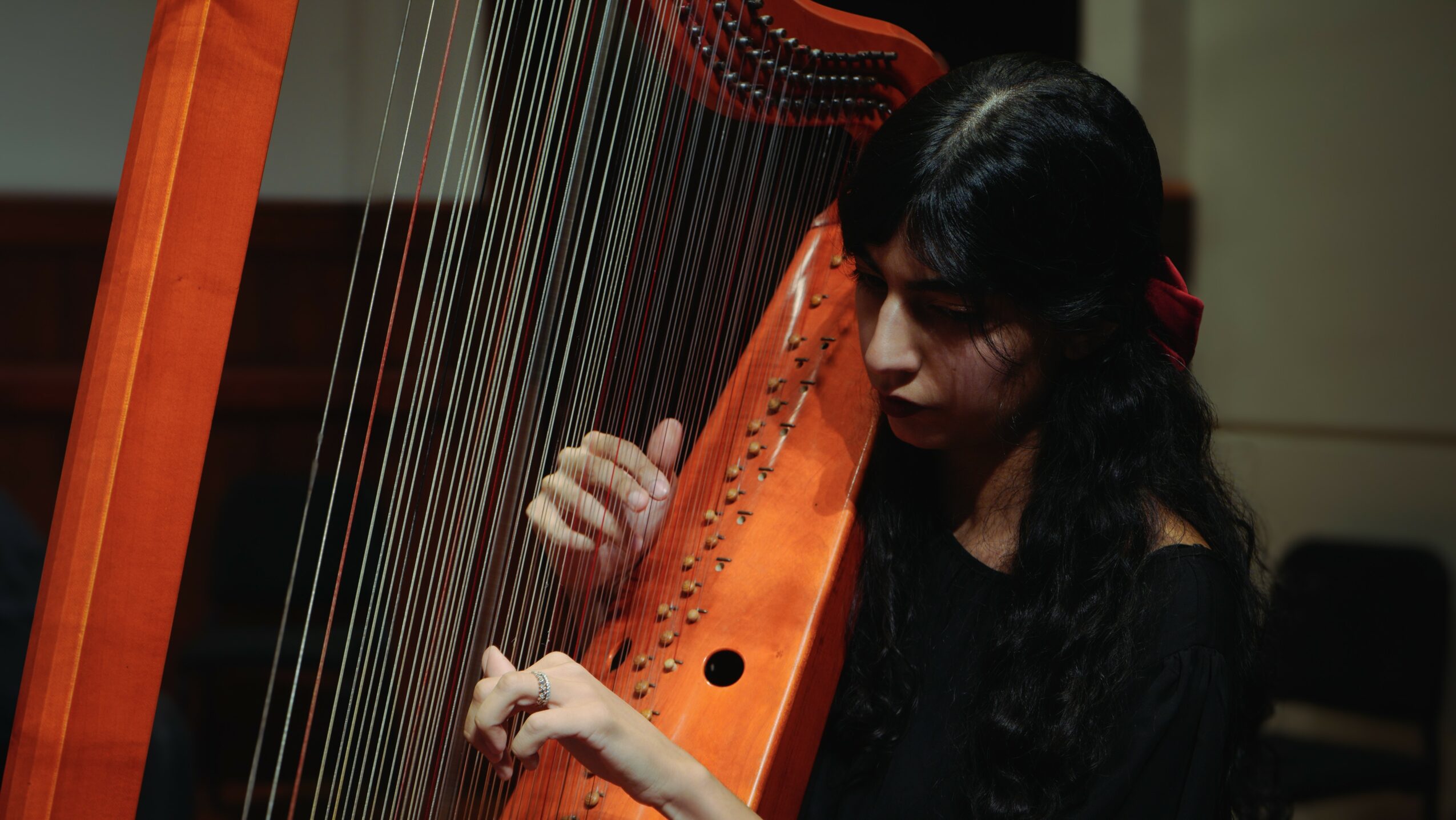Woman playing a harp, focusing on the strings and her hands, with dark hair and a black top.