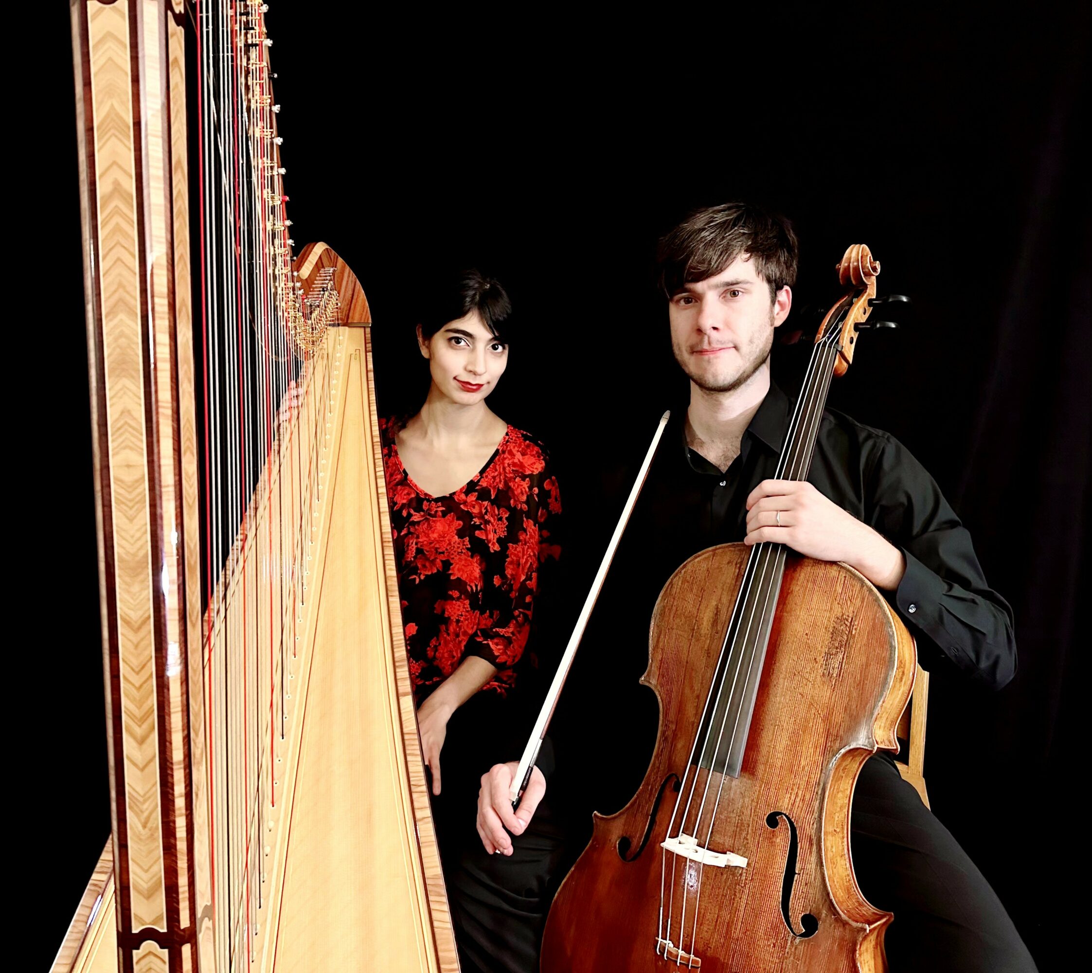 Two musicians, a woman and a man, with a harp and a cello, standing against a dark background.