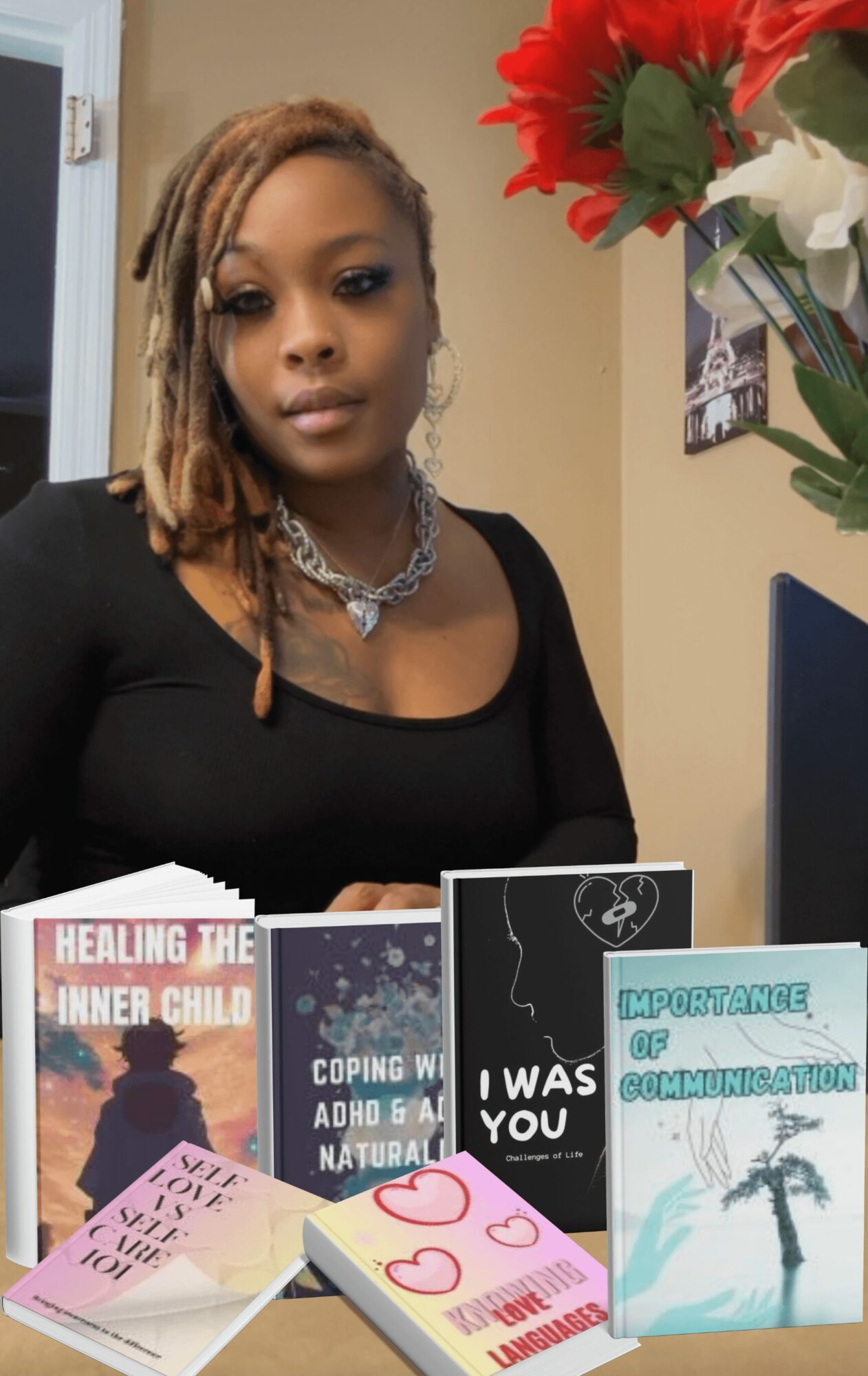 Woman with dreadlocks wearing a black top and necklace, sitting at a desk with books and a computer.