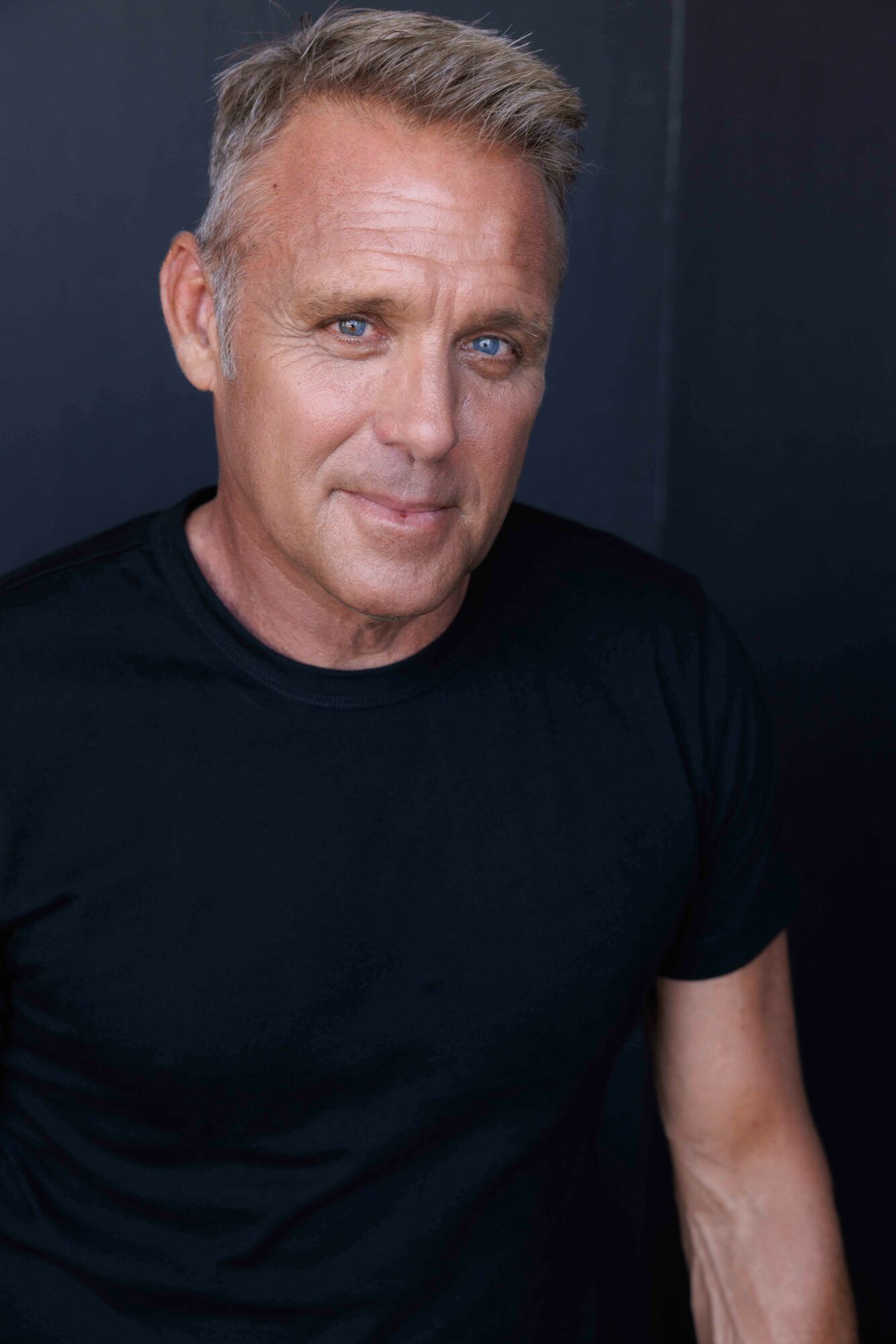Man with short gray hair and blue eyes wearing a black shirt, looking at the camera.