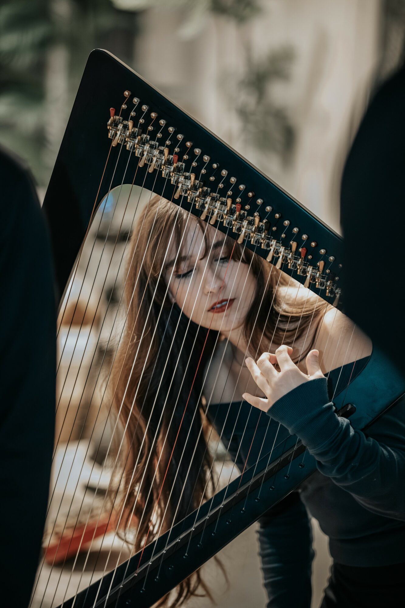 Young woman playing a harp outdoors, focusing on the strings and her hand, with blurred background.