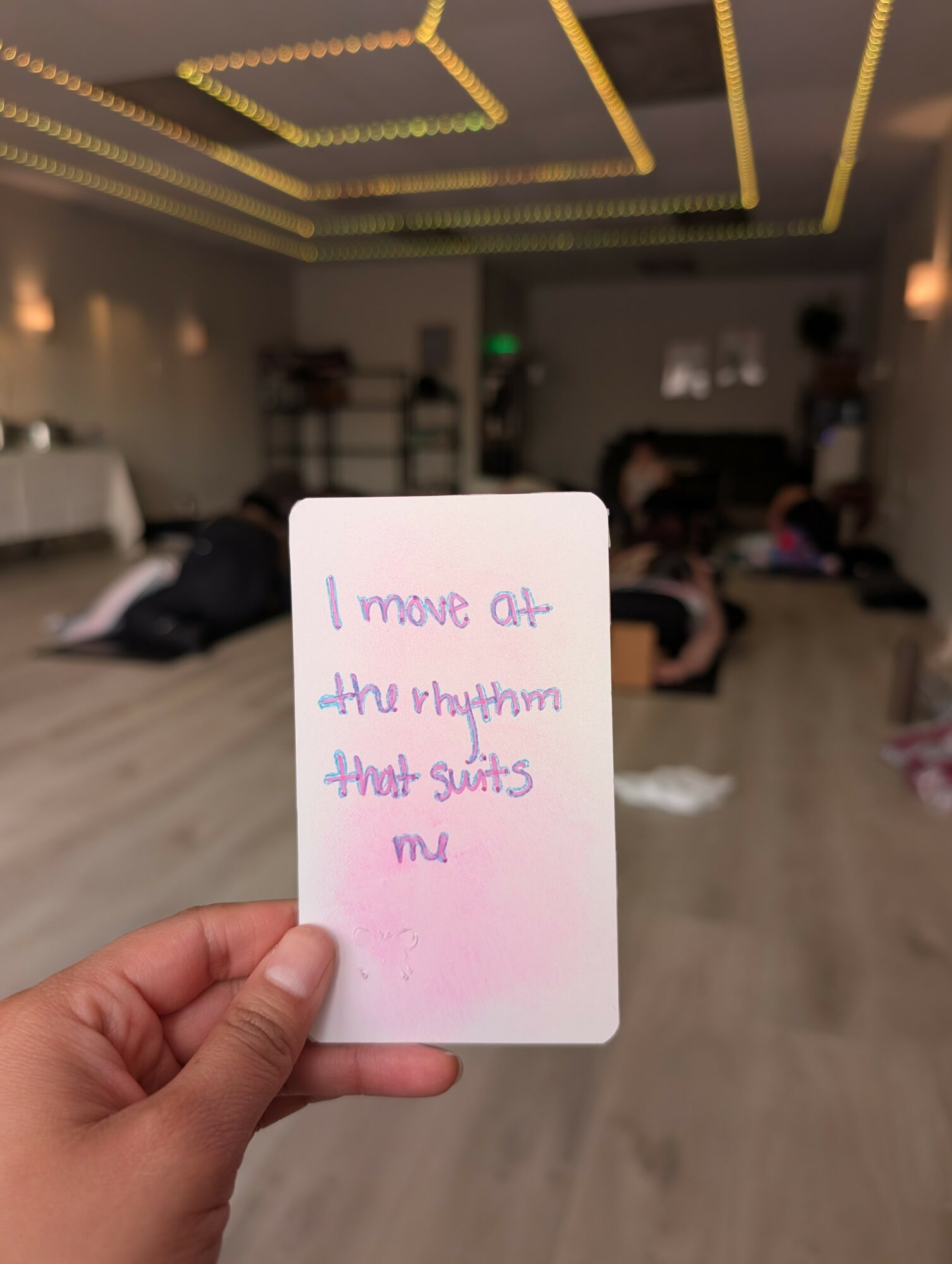 Person holding a note with handwritten text in a room with people and a decorated ceiling.
