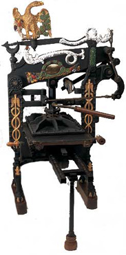 Ornate black and gold mechanical device with a small animal figure on top, featuring gears, levers, and decorative elements.