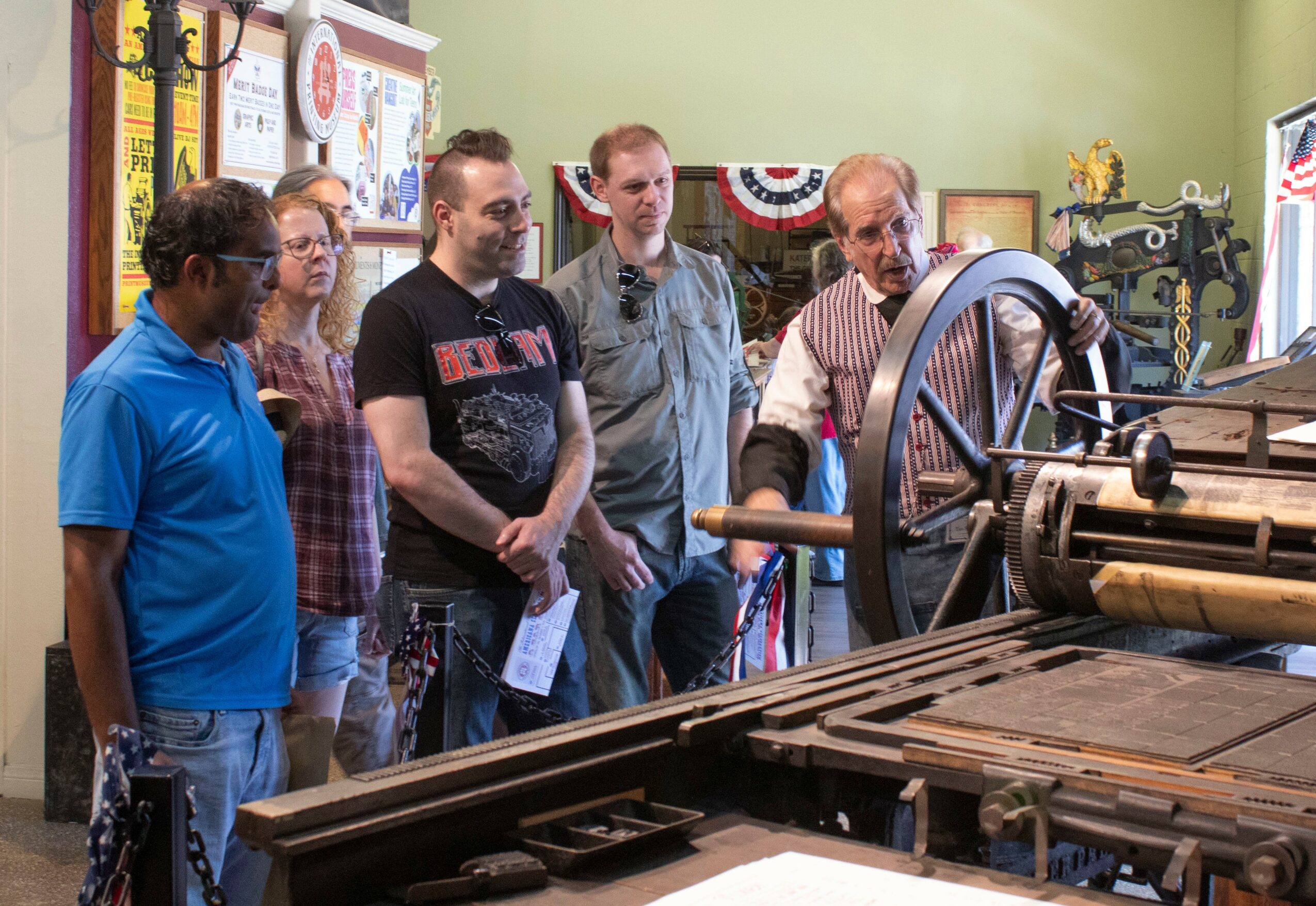 Group of five people observing a machine in a room decorated with patriotic bunting and vintage items.