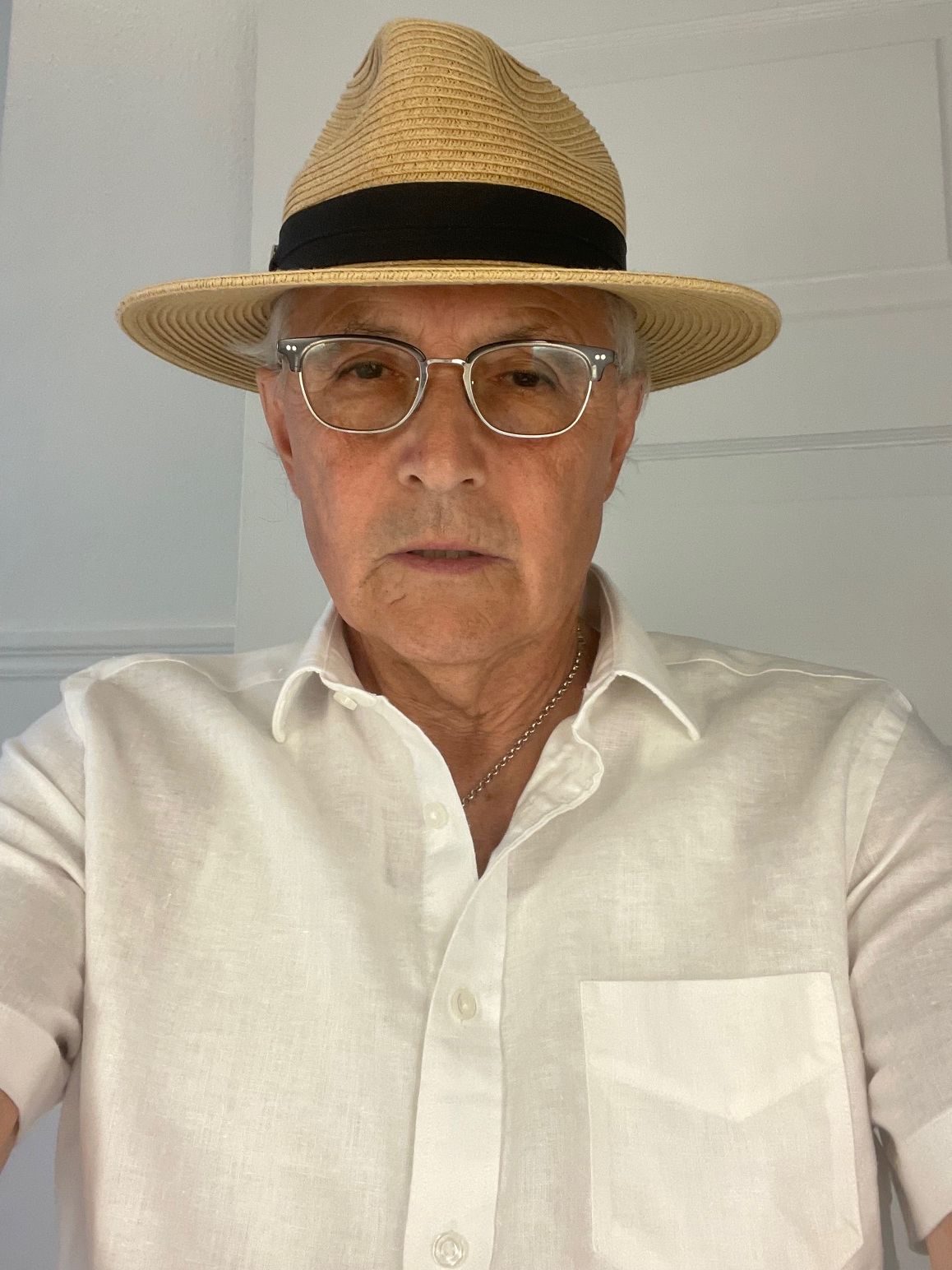 Man wearing glasses and a straw hat, dressed in a white shirt, looking at the camera.