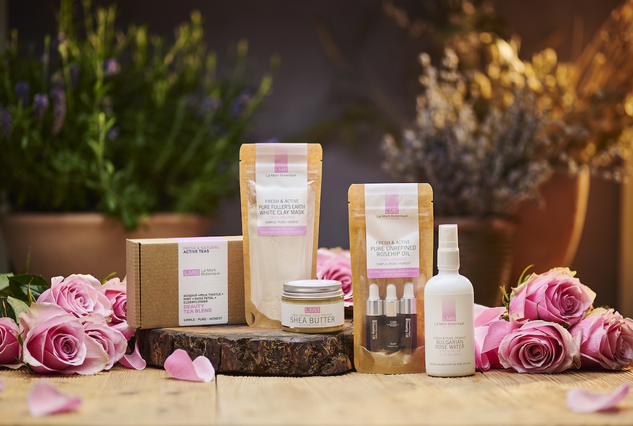 Skincare products and pink roses arranged on a wooden surface with plants in the background.