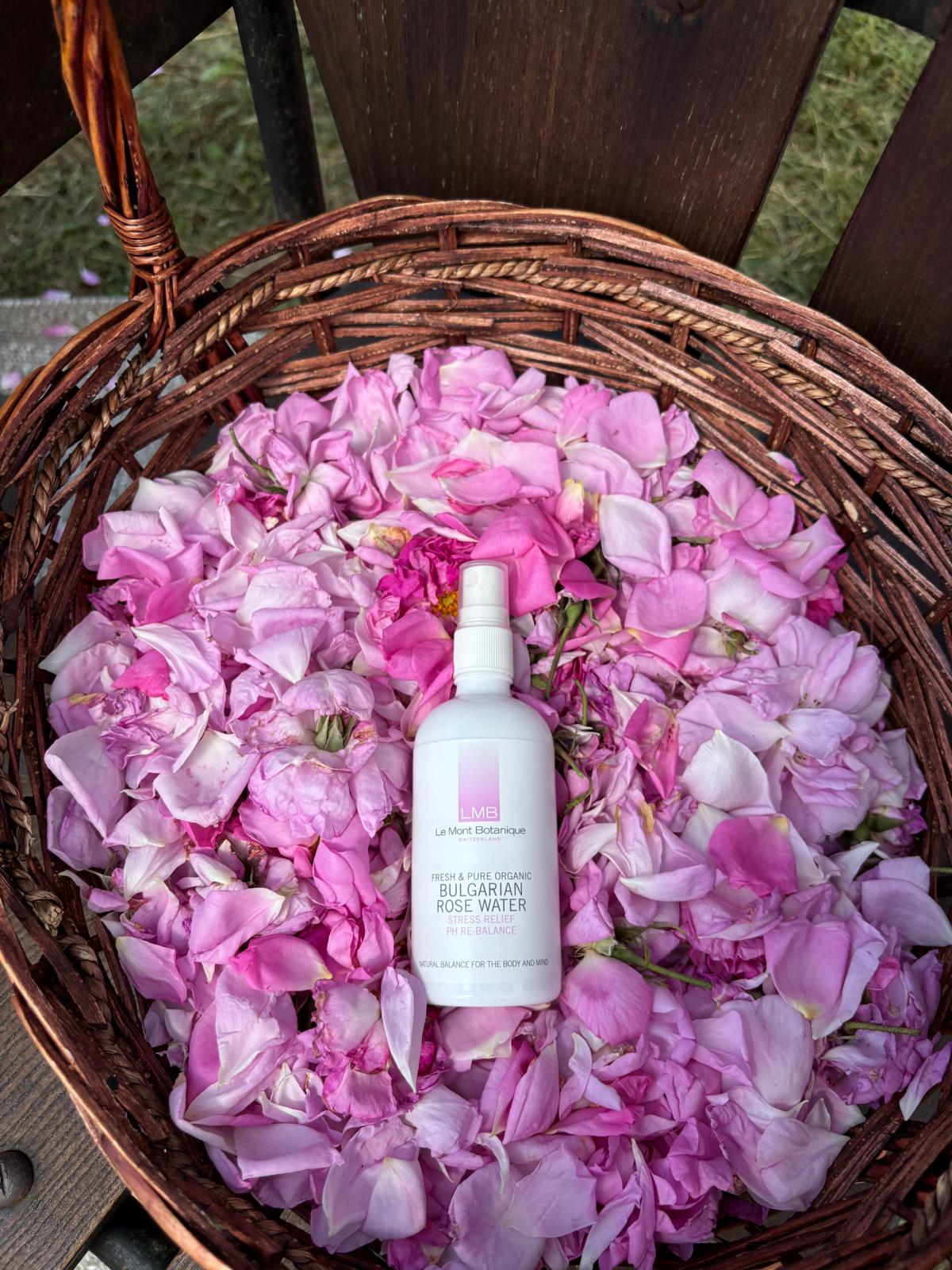 White spray bottle placed on pink and white flower petals inside a wicker basket, outdoors.