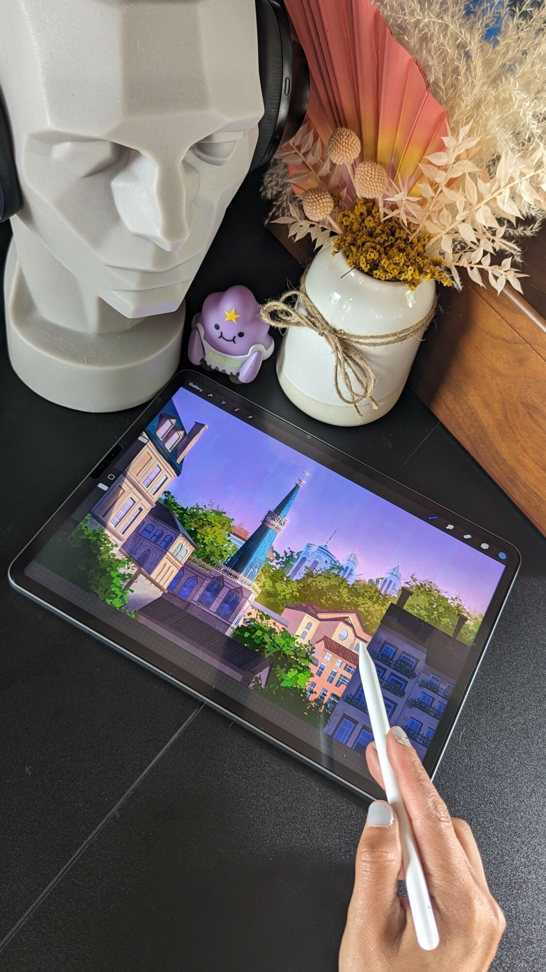 Tablet displaying a colorful cityscape with buildings and a tower, held by a person using a stylus, on a desk.