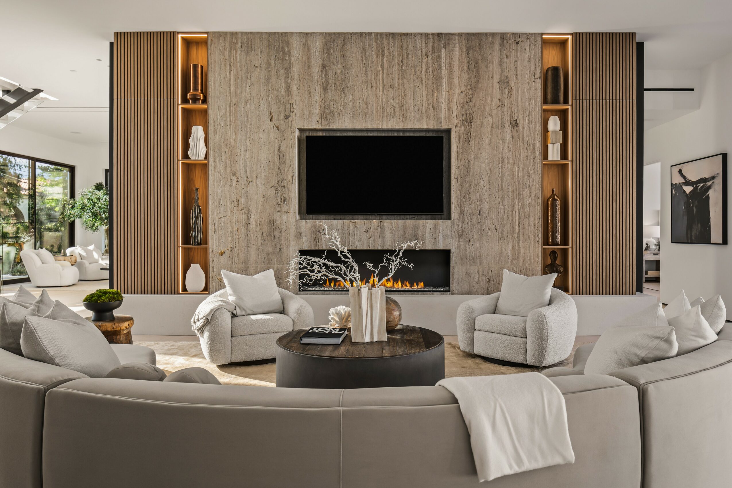 Living room with a large curved sofa, four armchairs, a central round table, and a wall-mounted TV, with built-in shelves on each side.