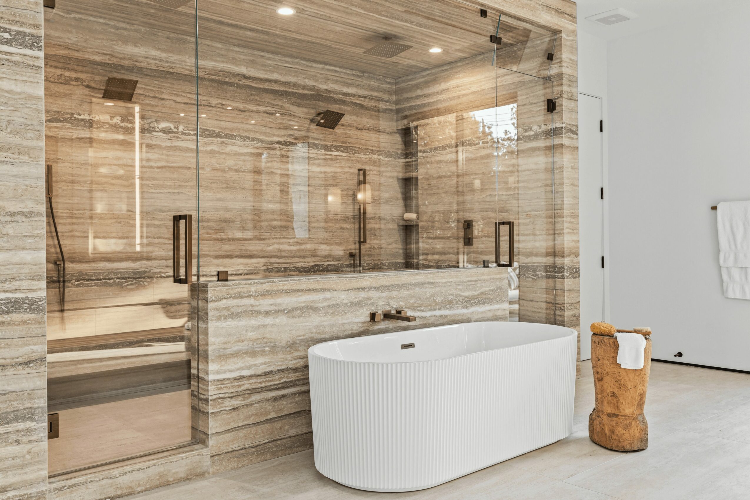 Bathroom with a freestanding bathtub, wooden wall, and glass shower enclosure, with a white wall and towel on the right.