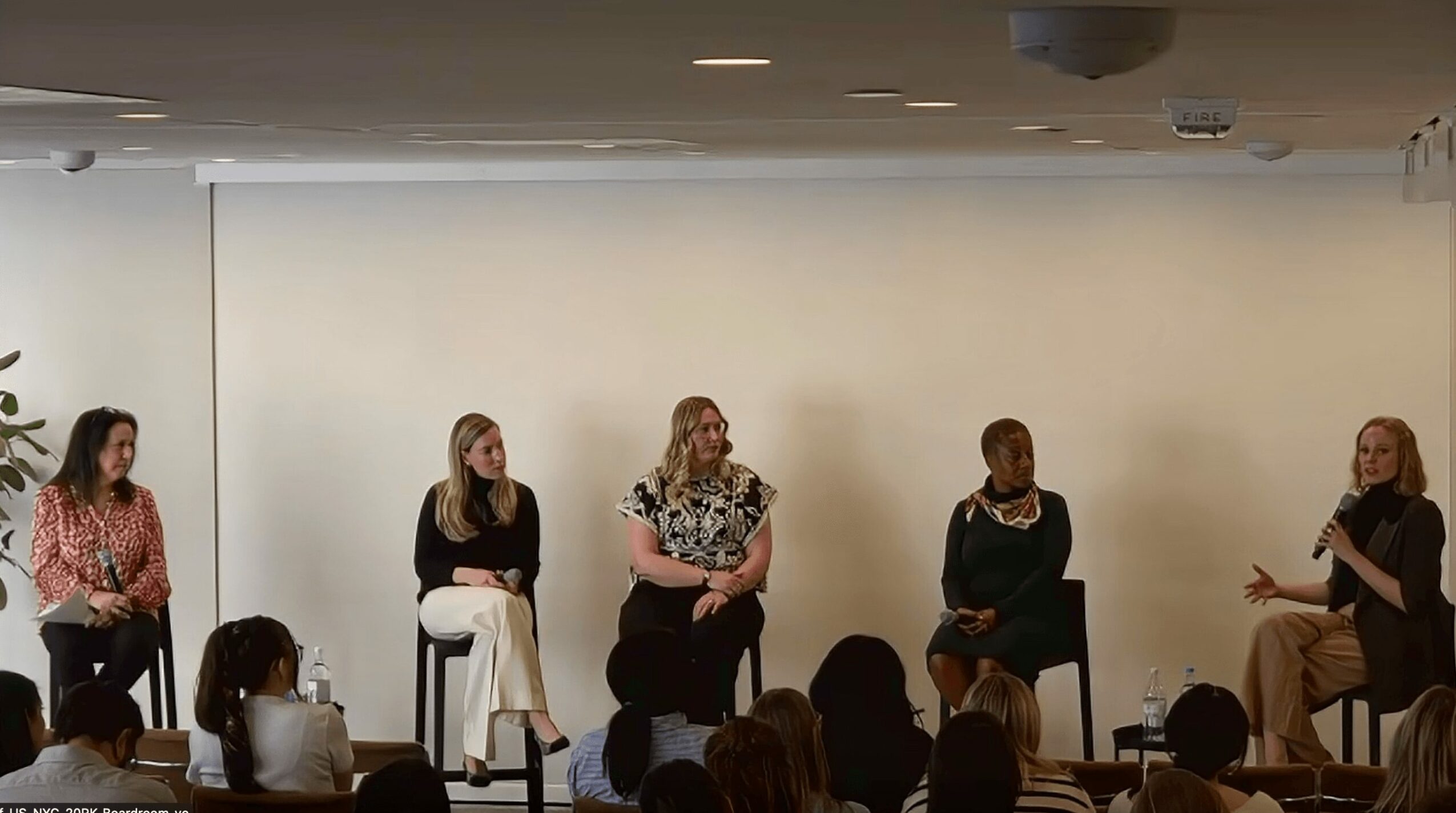 Five women seated on stage in front of an audience, engaging in a panel discussion or presentation.