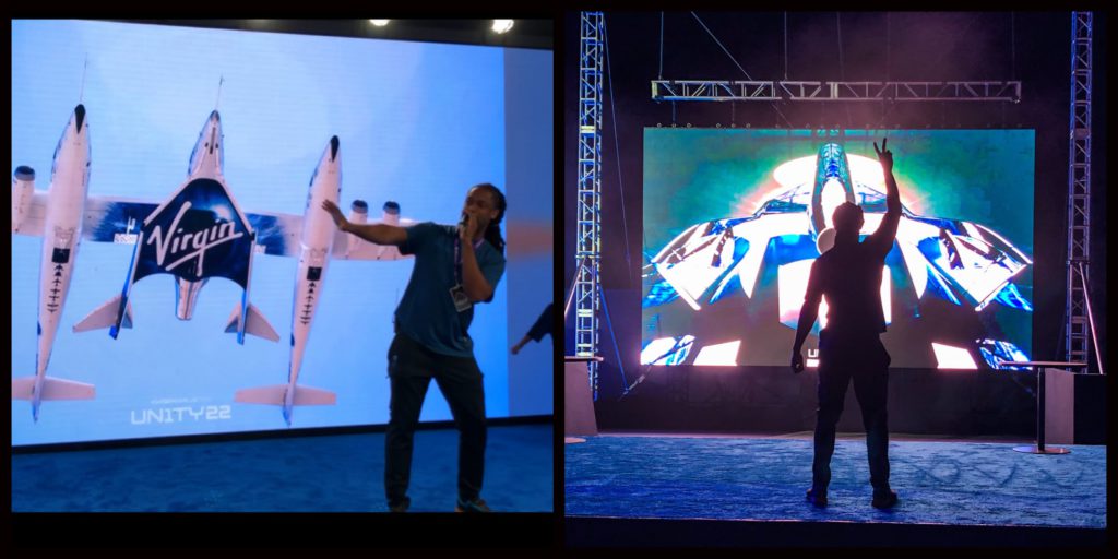 Person standing in front of large screen displaying Virgin Galactic spacecraft, with arms outstretched.