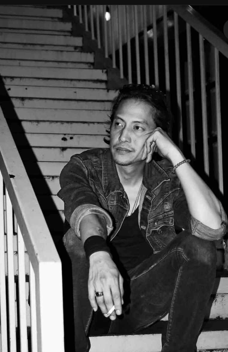 Person sitting on stairs with hand on face, looking to the side, in black and white.
