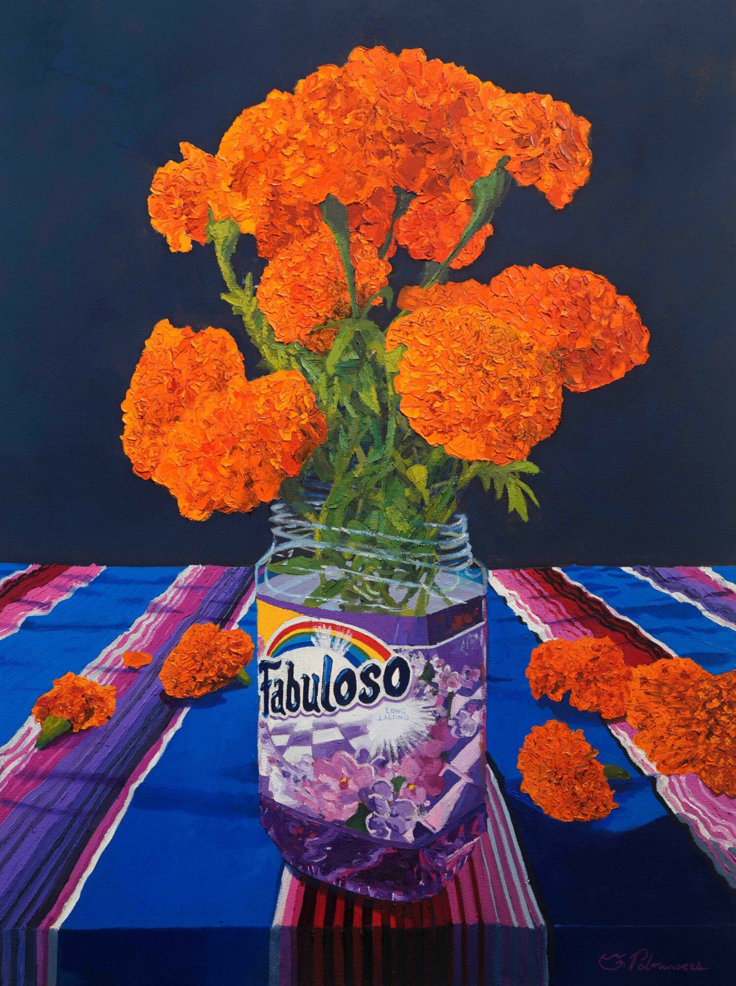 A jar labeled 'Fabuloso' holds orange marigold flowers, with some flowers and petals scattered on a colorful striped tablecloth.