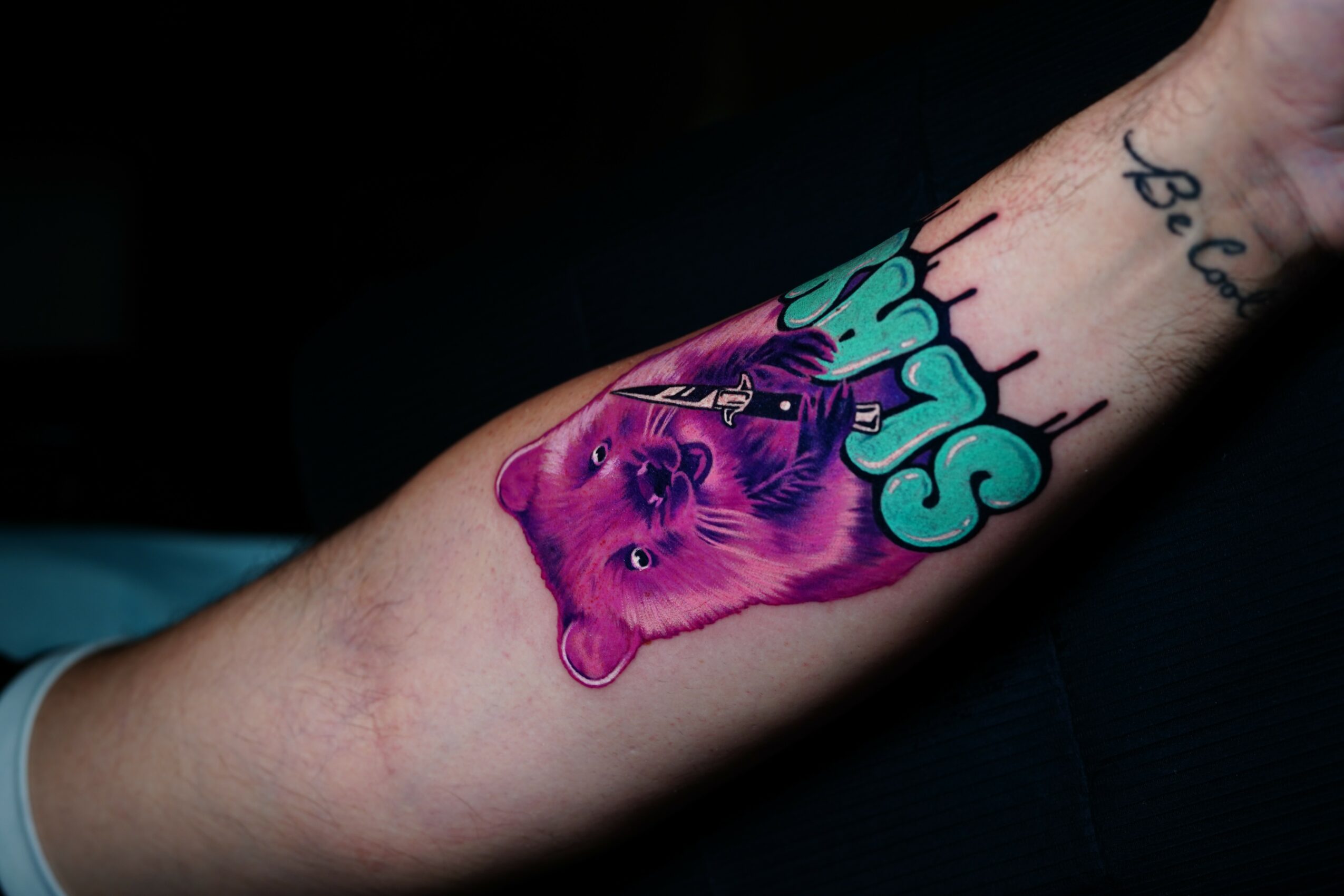 Tattoo of a purple lion's face with colorful text and design elements on a person's arm.