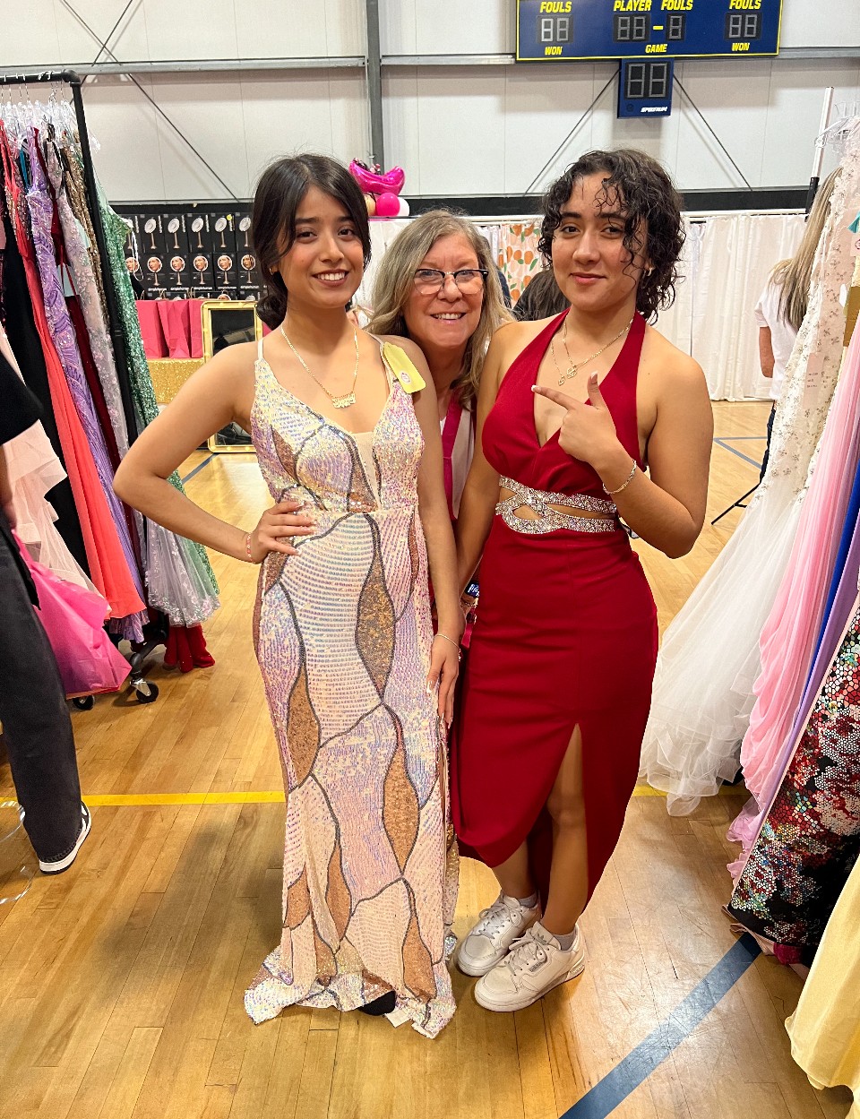 Three women standing together in a store, smiling, with dresses and fabric in the background.