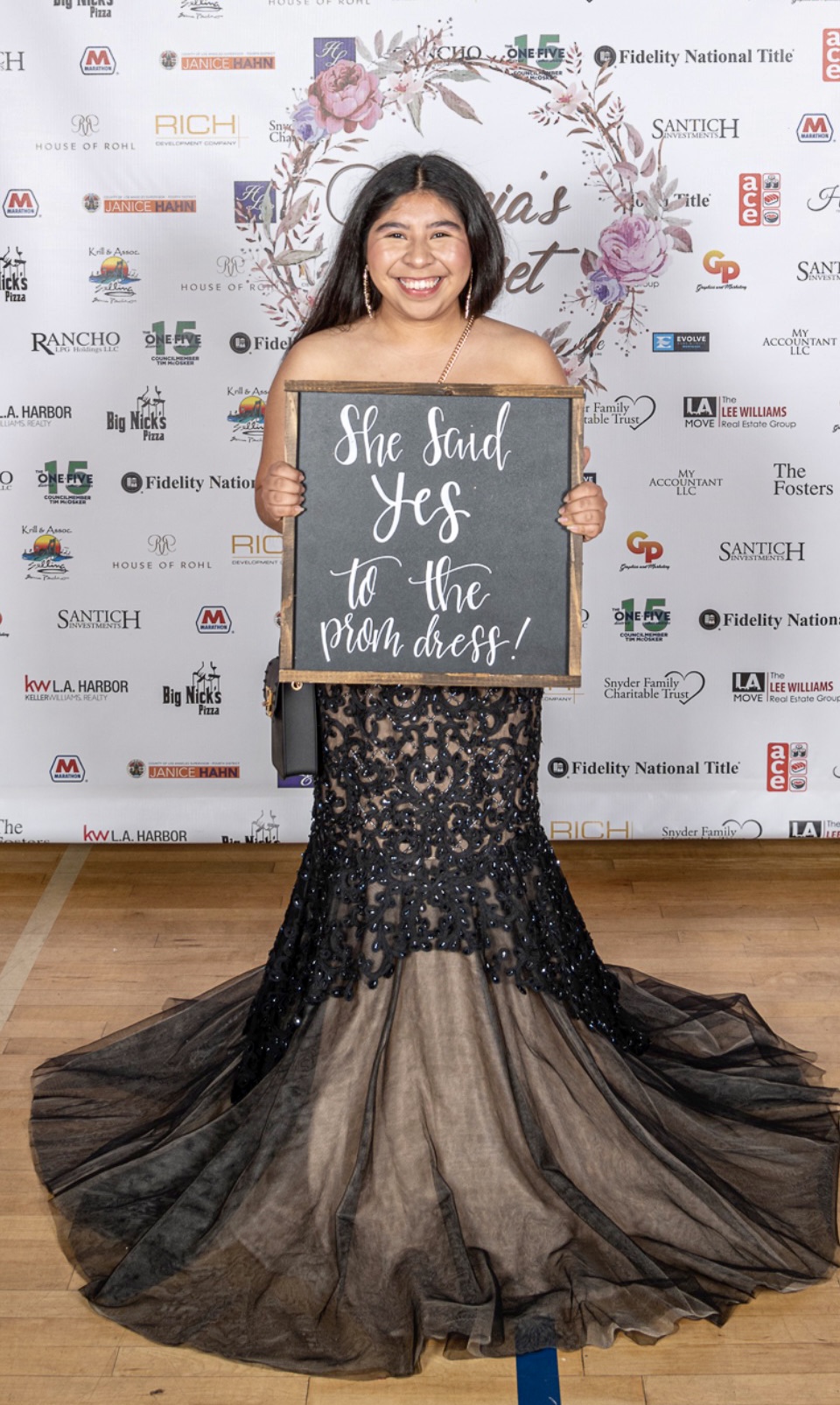 Young woman in a black and gold gown holding a sign that says,