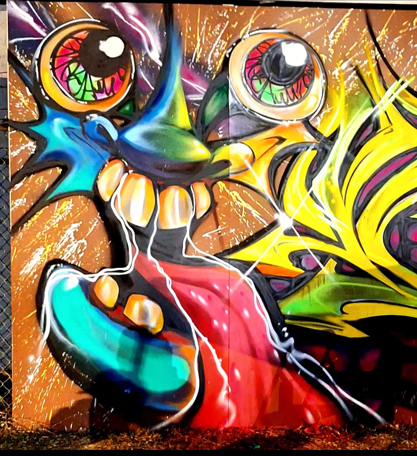 Colorful graffiti of a cartoonish creature with large eyes, a wide mouth, and vibrant colors, on a wall.