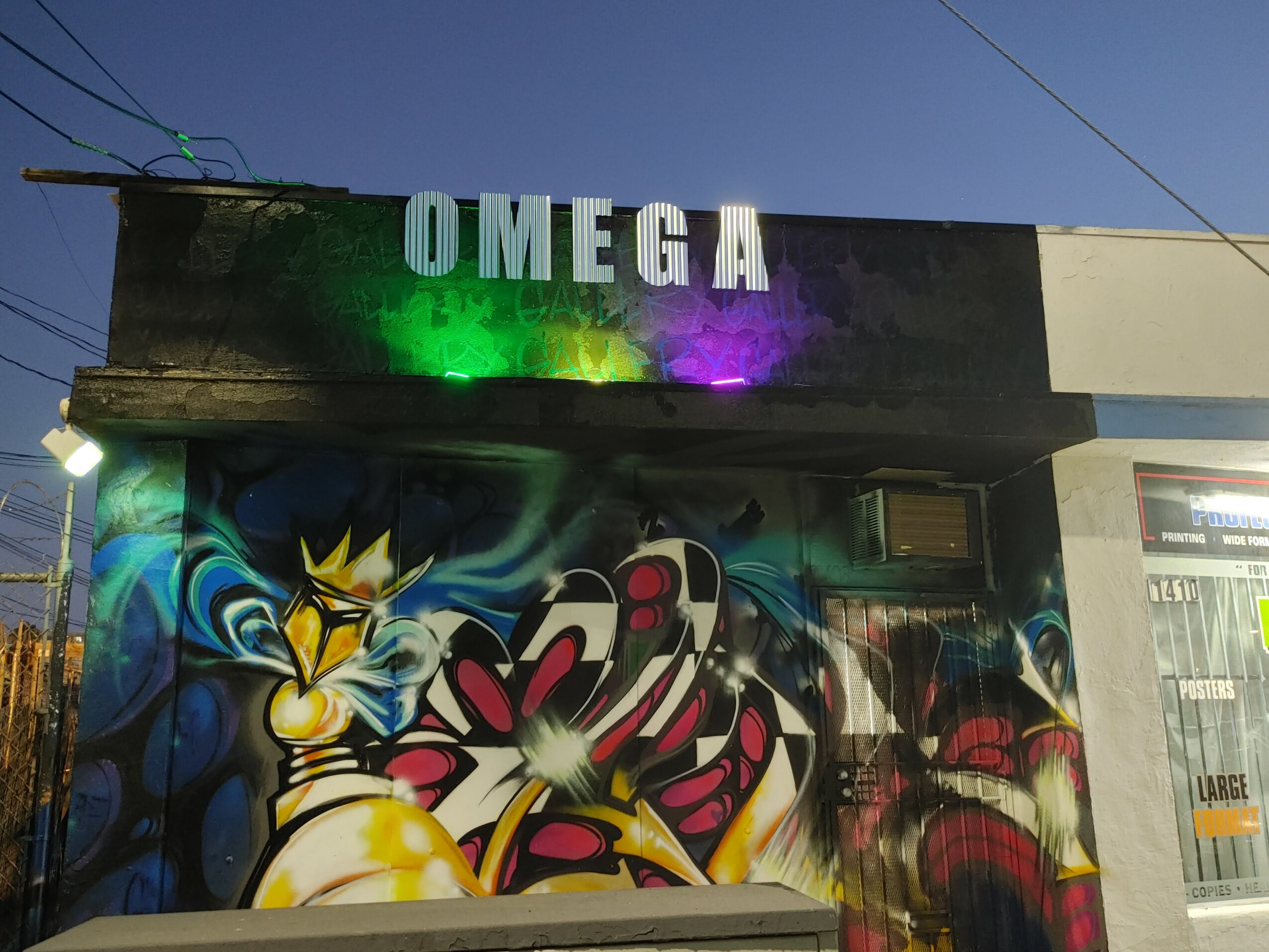Building with a colorful graffiti mural and a sign reading 'OMEGA' on top, under a clear blue sky.