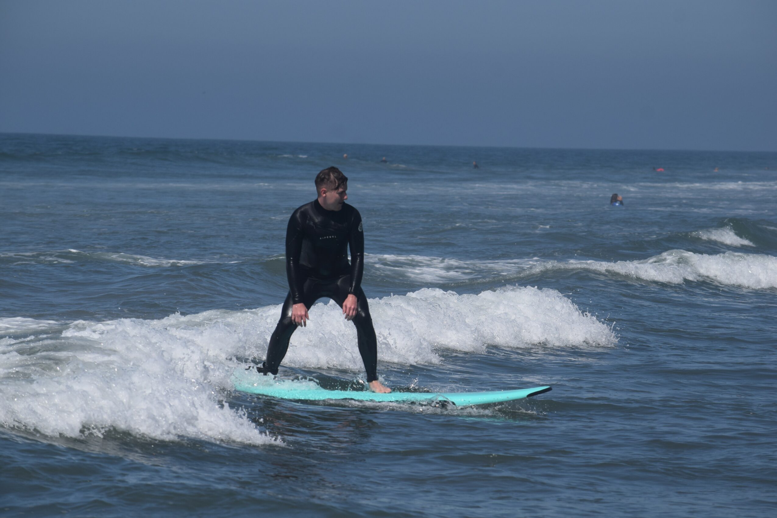Person standing on a surfboard riding a wave in the ocean, with a cloudy sky in the background.